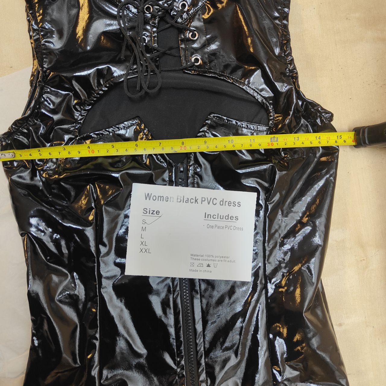 Black PVC dress with a measuring tape and size label on a beige background