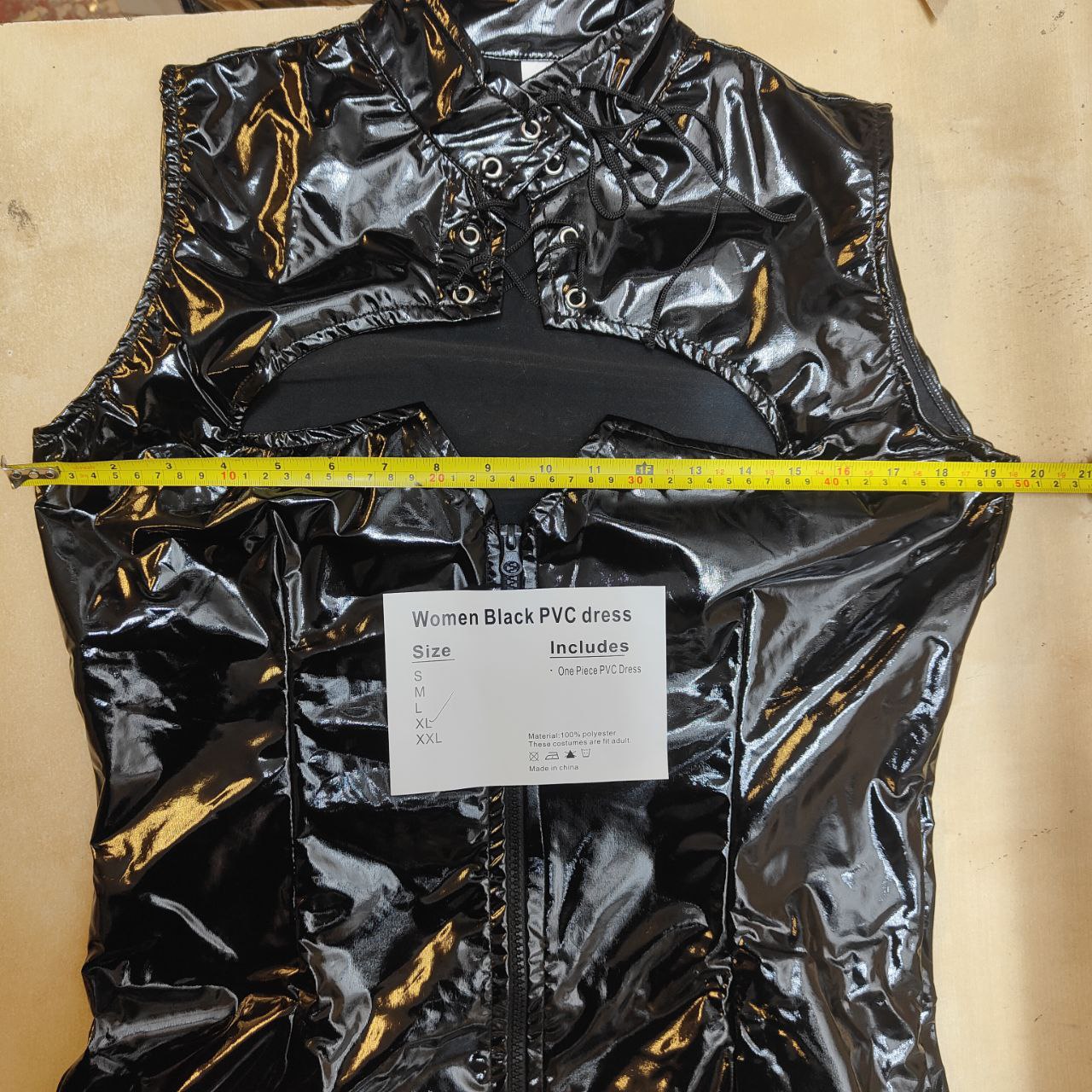 Black PVC dress with a measuring tape and label on a beige background