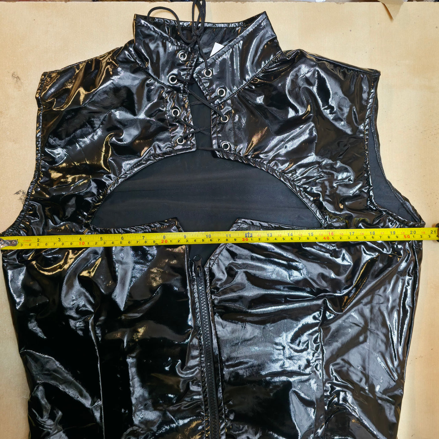 Black shiny vest with a measuring tape for size on a beige background