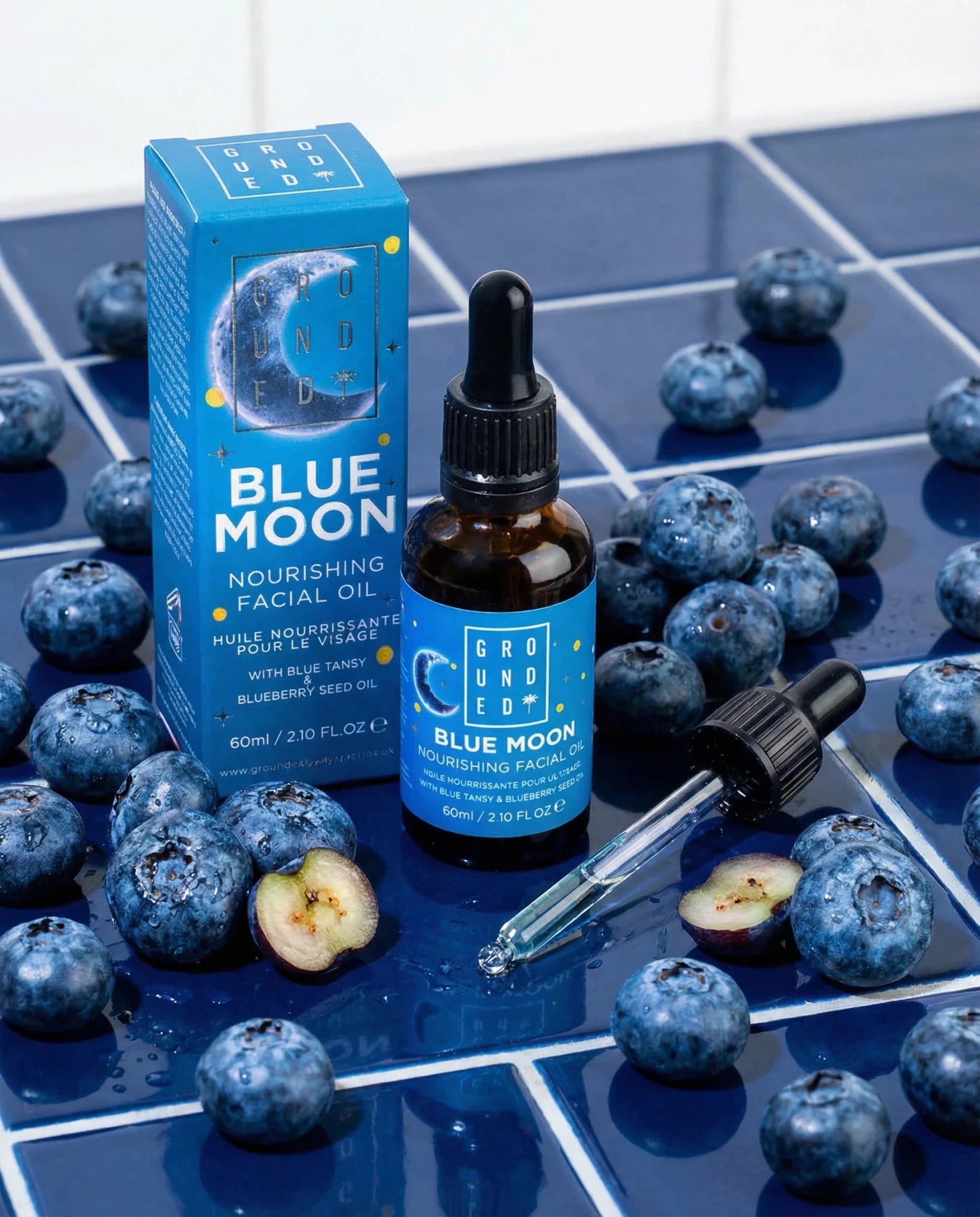 Blue Moon facial oil with packaging and blueberries on a checkered surface