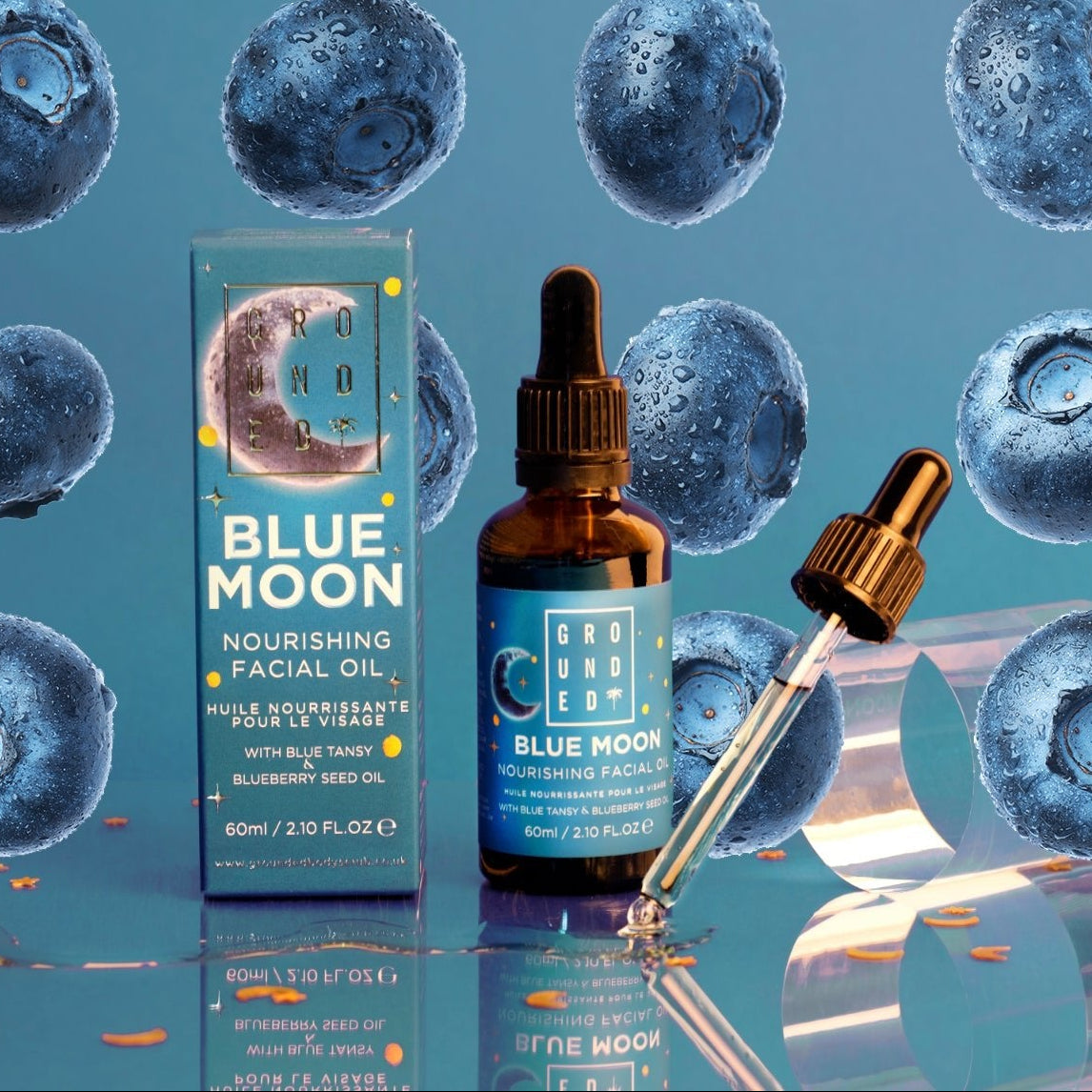 Blue Moon nourishing facial oil with packaging and dropper on a blue background with blueberries.