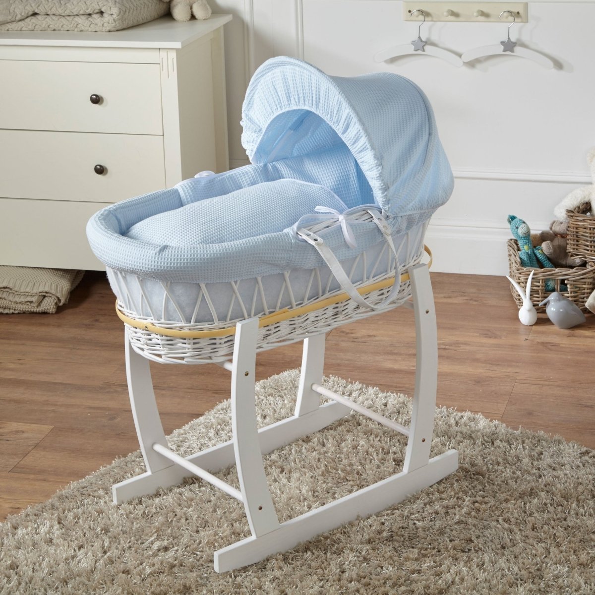 White wicker Moses basket with blue hood and lining in a nursery setting.