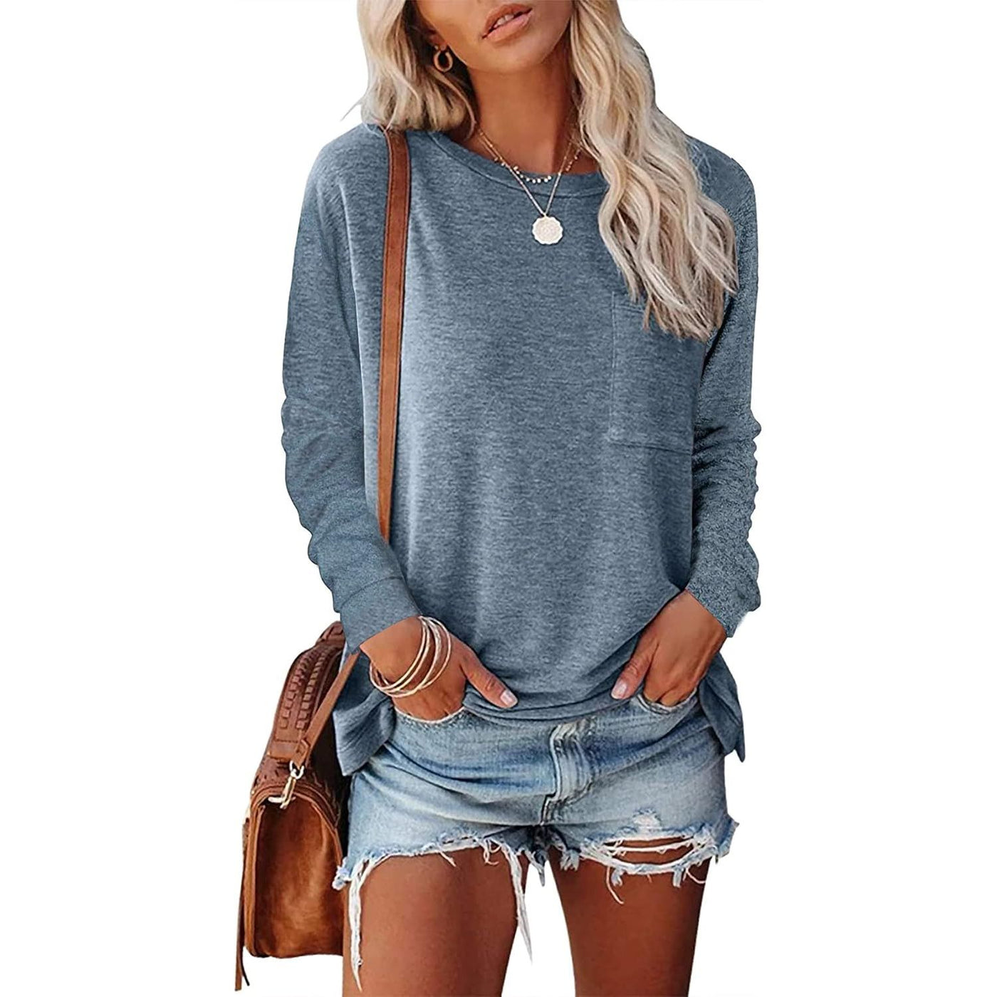 Woman wearing a blue long-sleeve top and denim shorts with a brown leather bag on a white background
