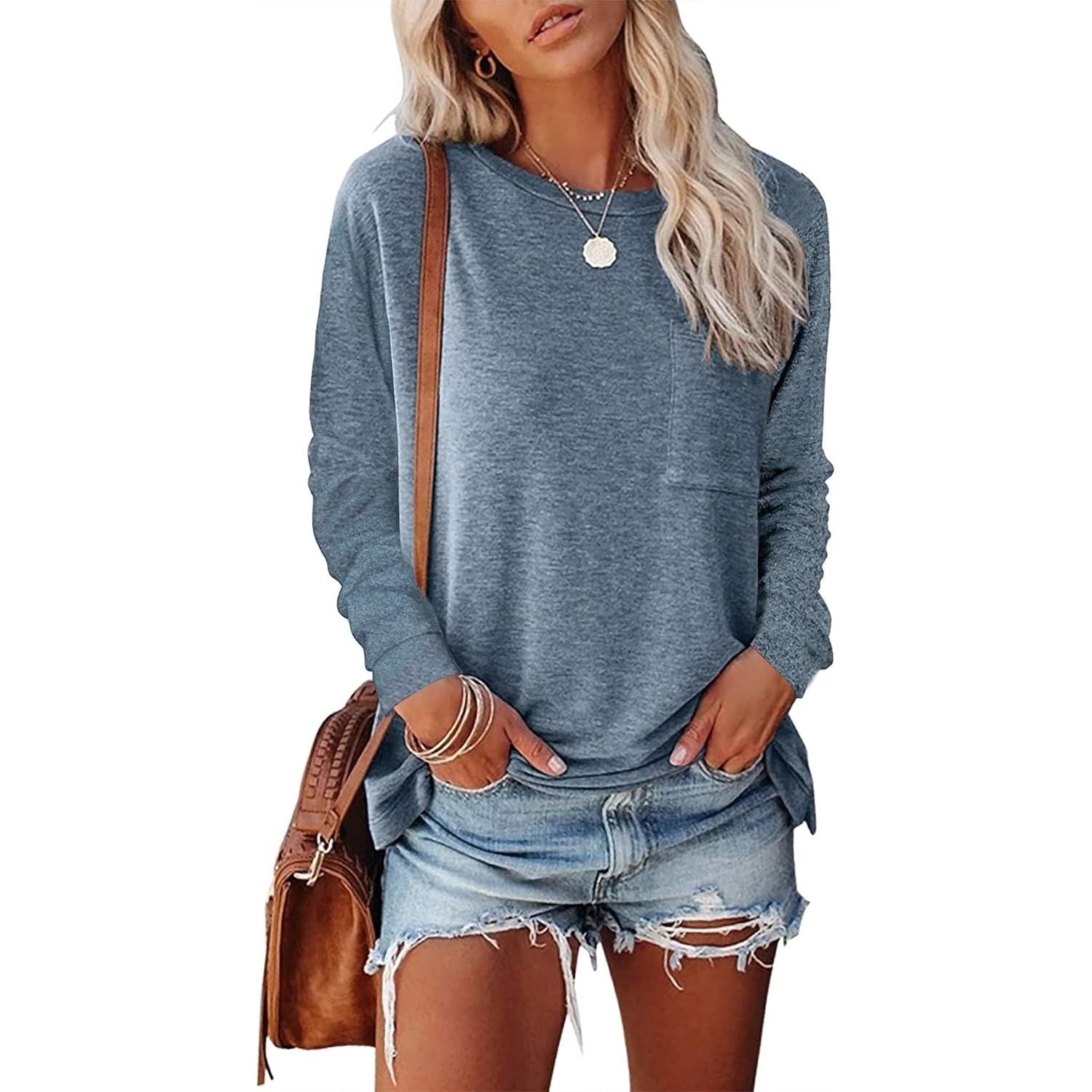 Woman wearing a blue long-sleeve top and denim shorts with a brown leather bag on a white background