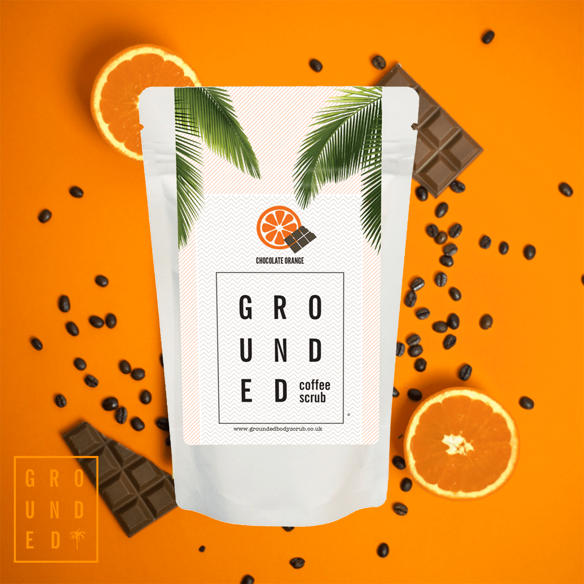 Grounded coffee scrub package on an orange background with chocolate and oranges.