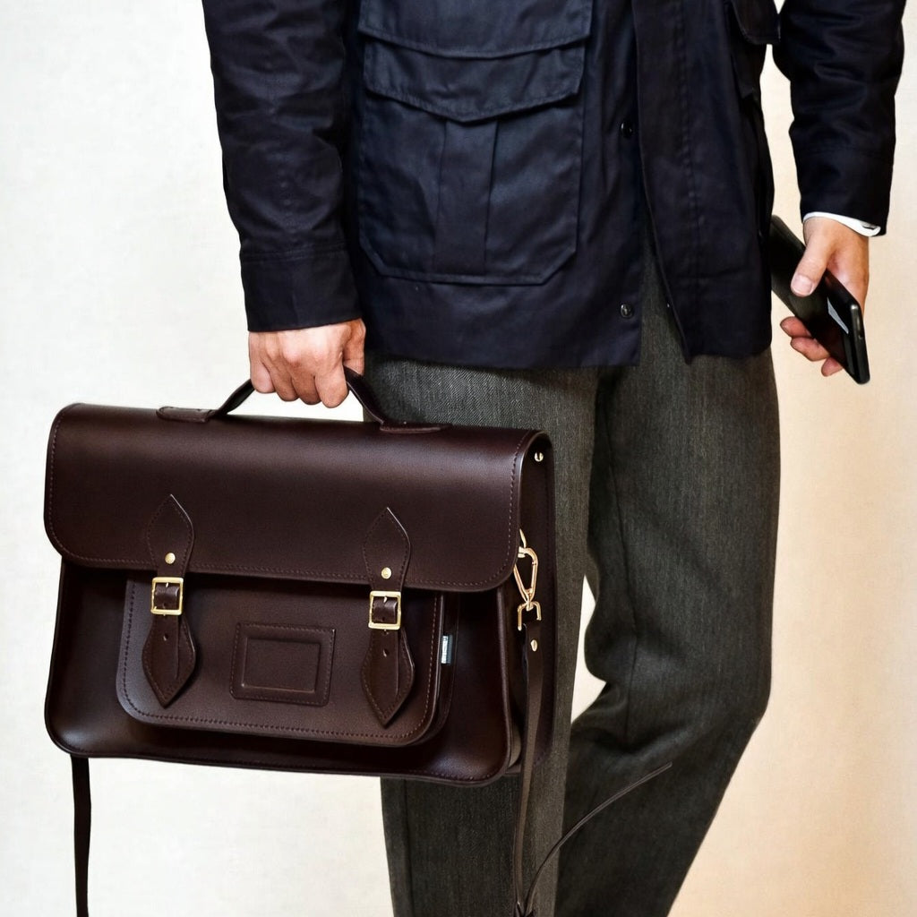 Person holding a brown leather satchel bag with a neutral background