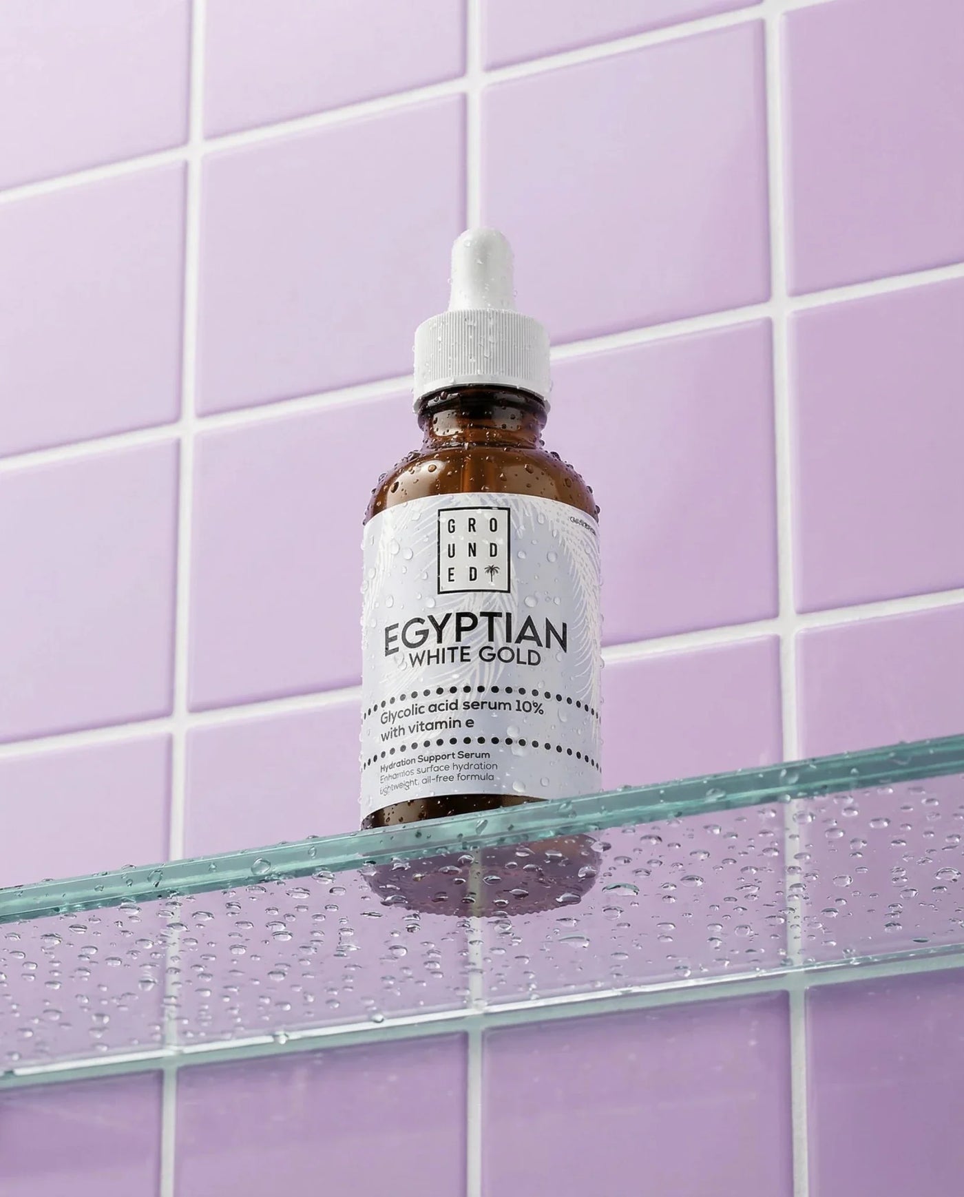 Bottle of 'Egyptian White Gold' serum on a glass shelf against a purple tiled wall.