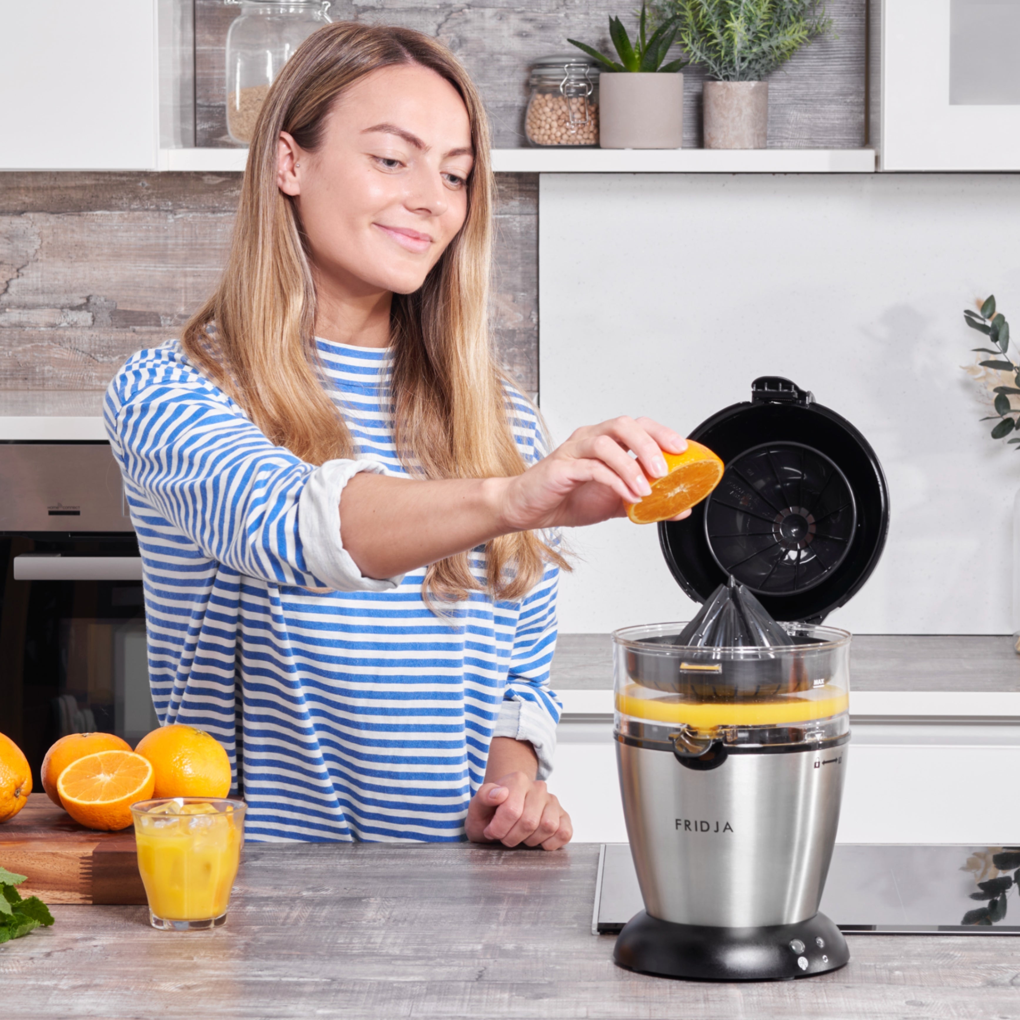 Woman using a juicer to make orange juice in a kitchen.