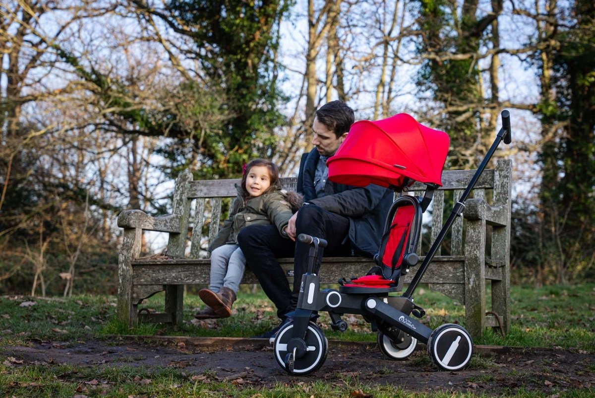 Man and child sitting on a bench with a red stroller in a park setting