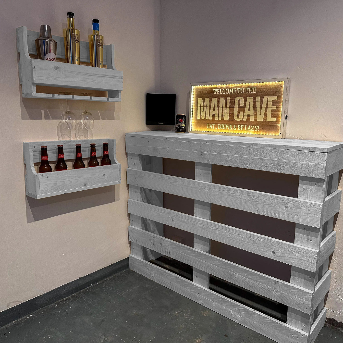 Man cave setup with wooden shelves, bottles, and a 'Welcome to the Man Cave' sign.