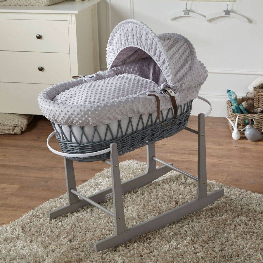 Gray wicker baby Moses basket with hood on a stand in a room setting.