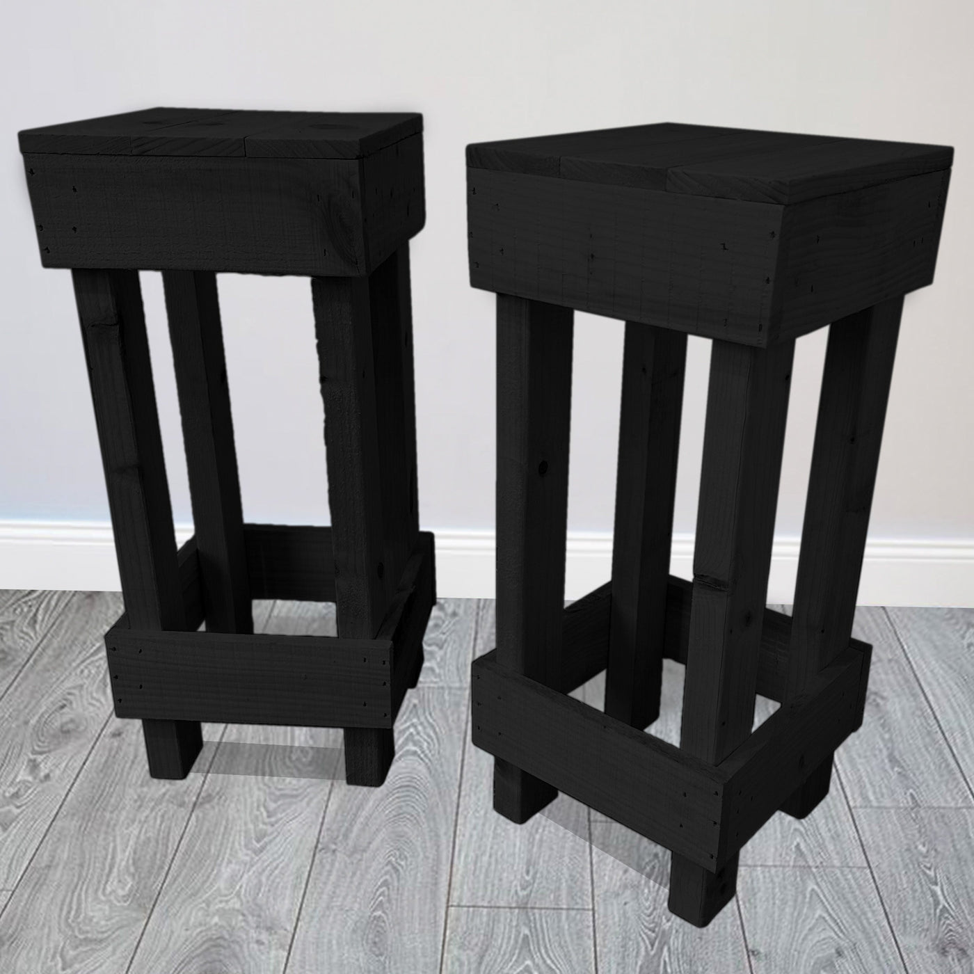 Two black wooden stools on a gray wooden floor with a white wall background.