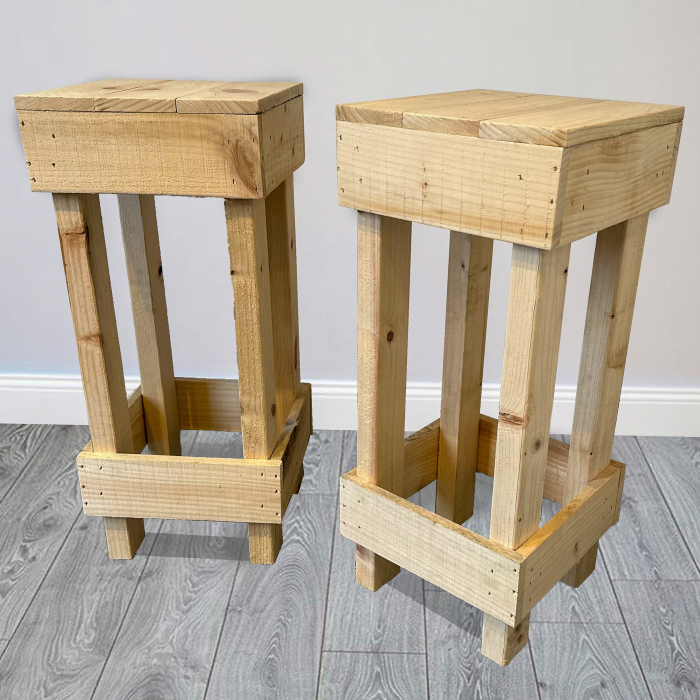 Two wooden stools on a gray wooden floor with a plain white wall background.