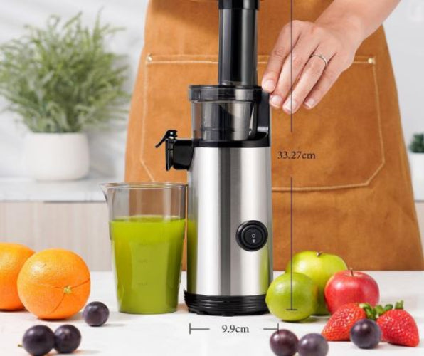 Juicer with a glass of green juice, fruits, and measurements on a white surface.