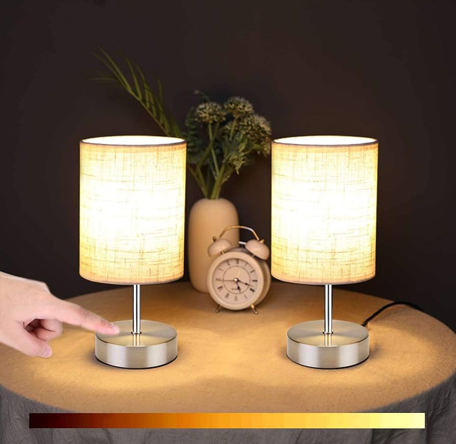 Two table lamps on a surface with a hand pointing at one of them, against a dark background.