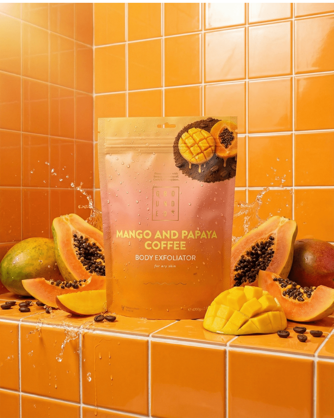 Mango and papaya coffee body exfoliator packaging on an orange tiled background with mangoes and papayas.