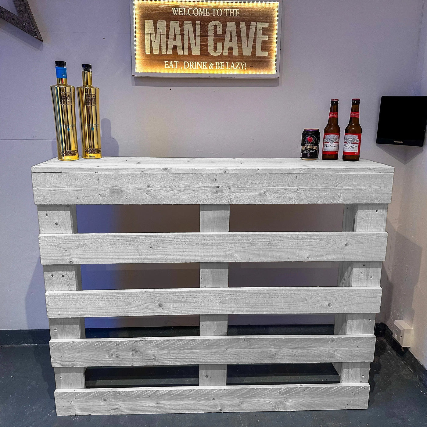 Wooden pallet bar with bottles against a wall with a 'Man Cave' sign.