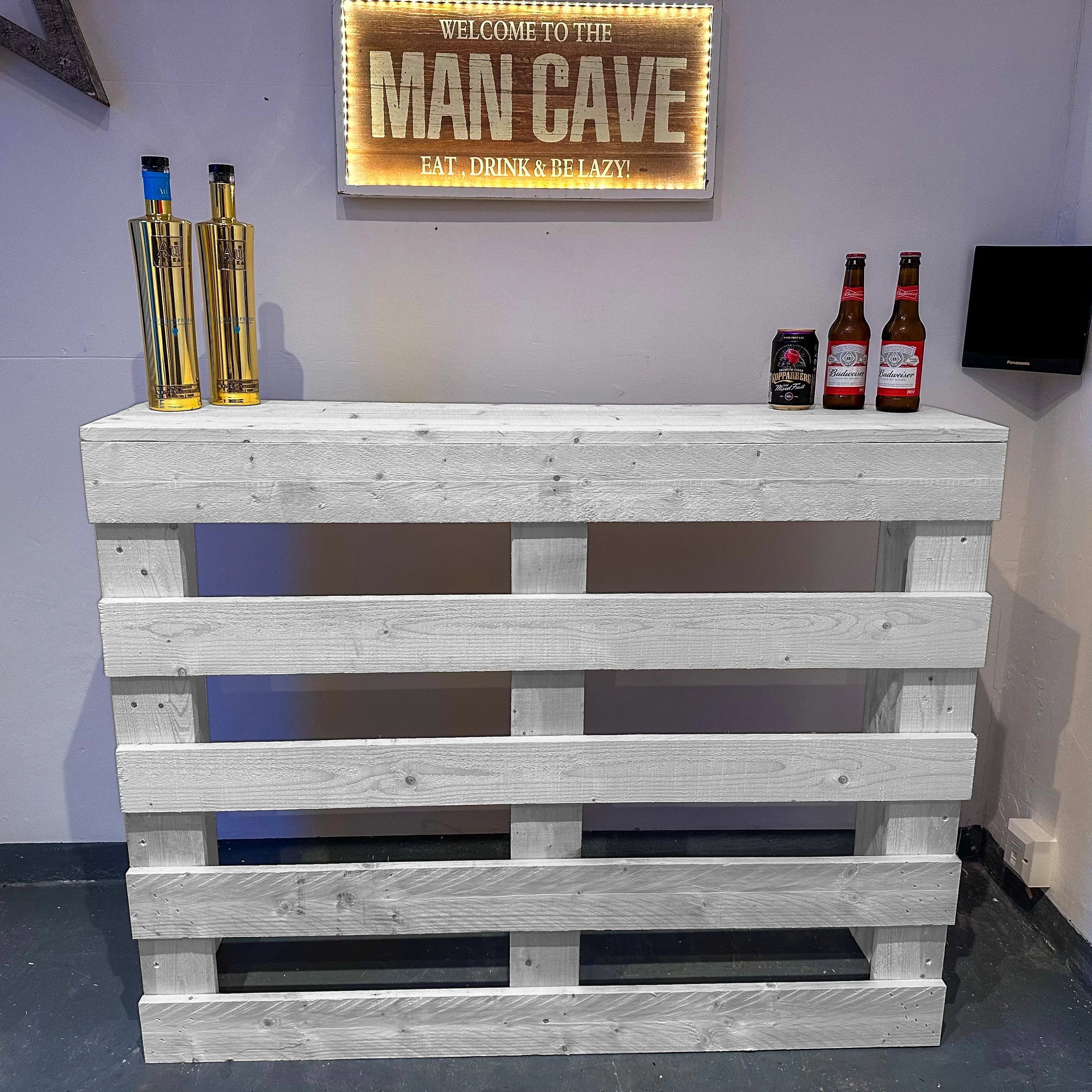 Wooden pallet bar with bottles against a wall with a 'Man Cave' sign.