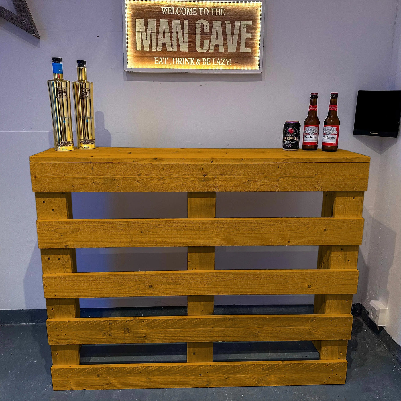 Wooden pallet bar with bottles and a 'Man Cave' sign on a wall.