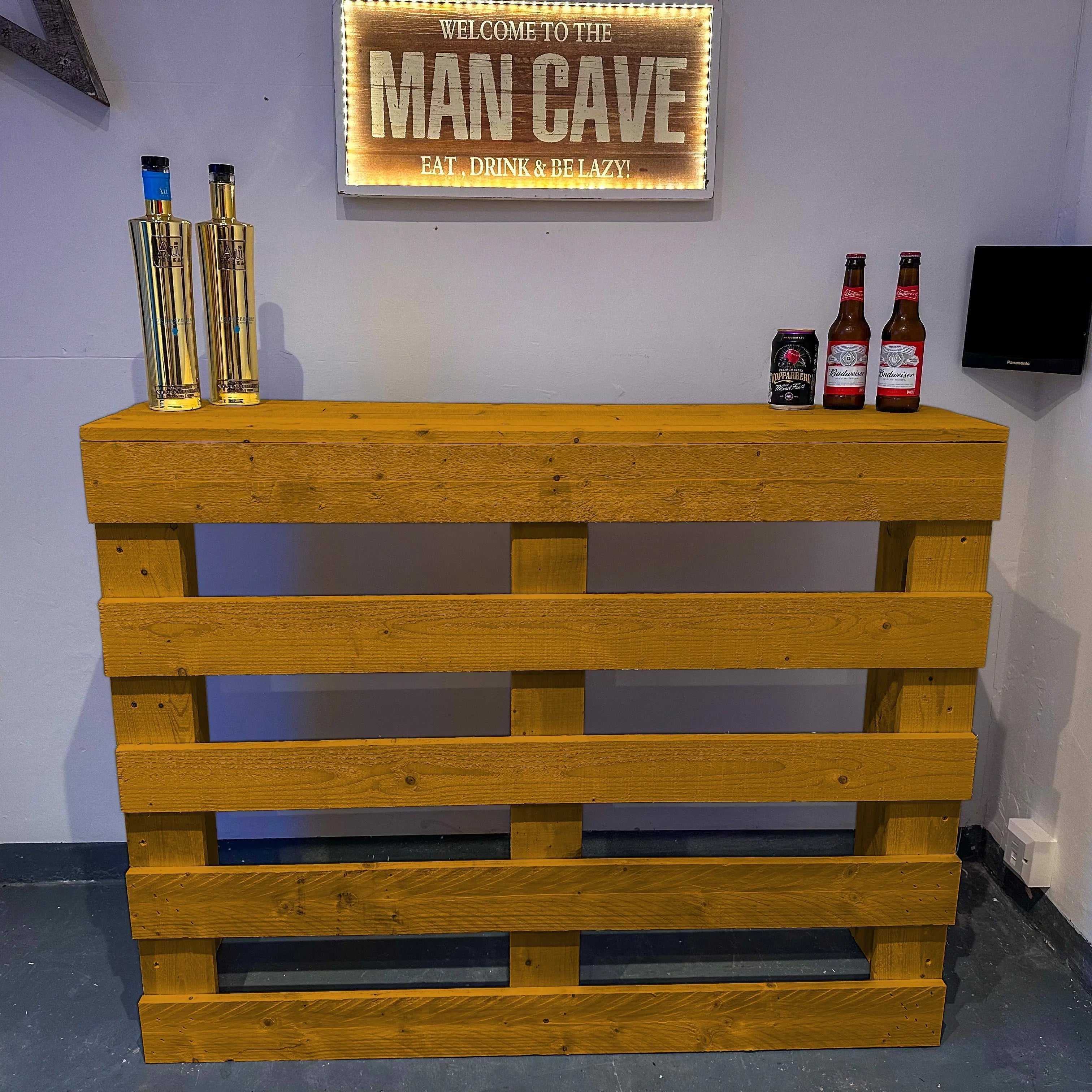Wooden pallet bar with bottles and a 'Man Cave' sign on a wall.