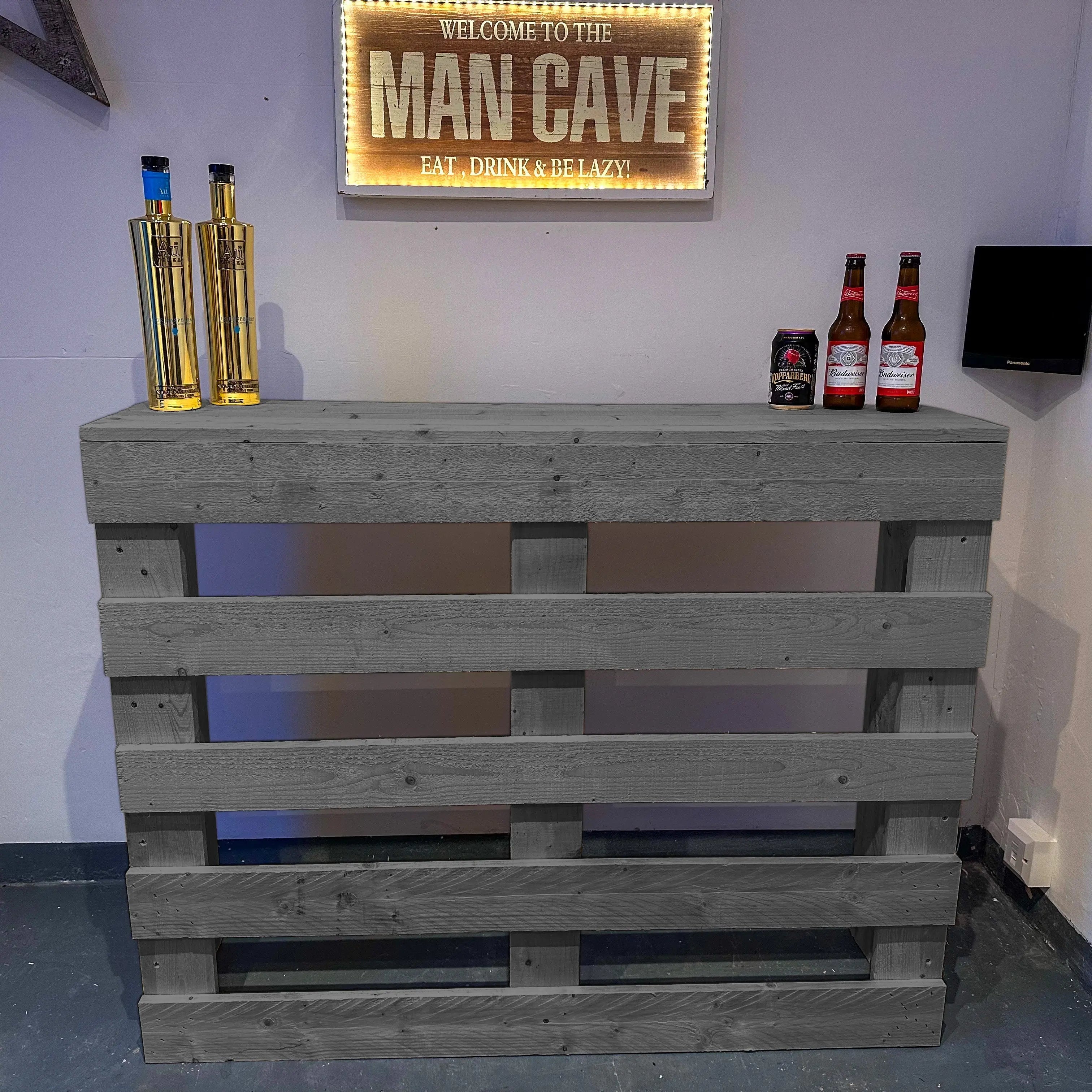 Wooden pallet bar with bottles against a wall with a 'Man Cave' sign.