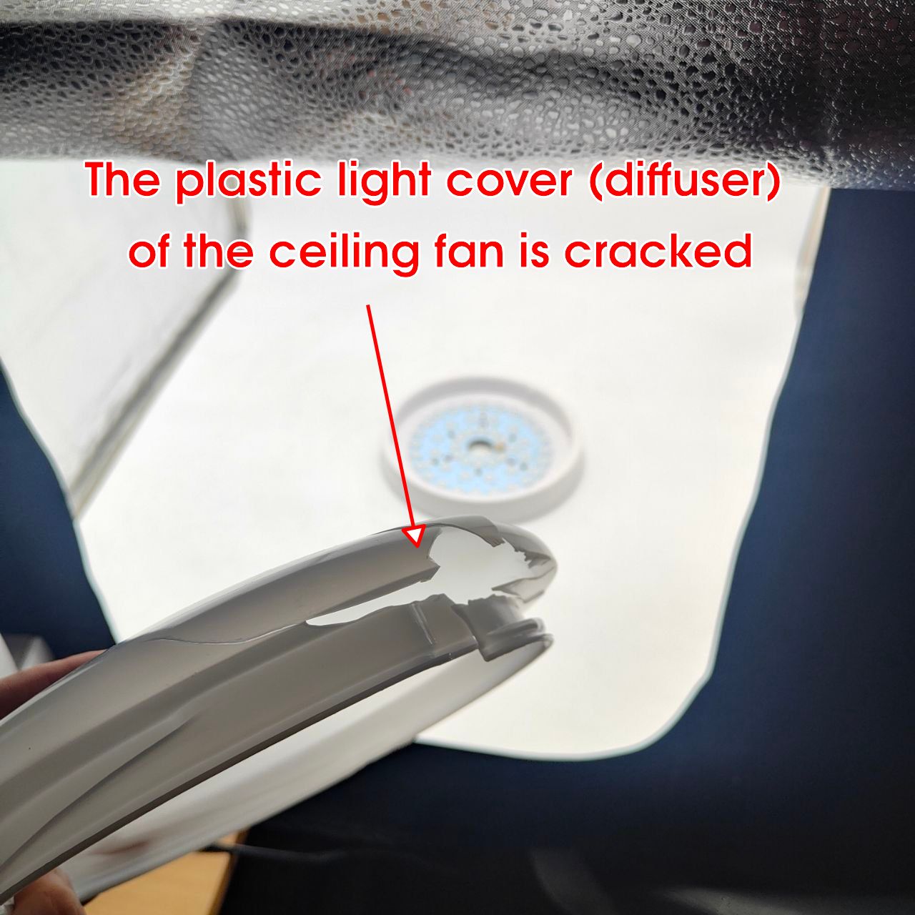 Cracked plastic light cover of a ceiling fan with text indicating the issue.