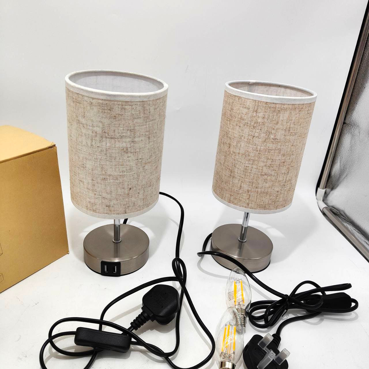 Two table lamps with beige lampshades and metal bases on a white surface.
