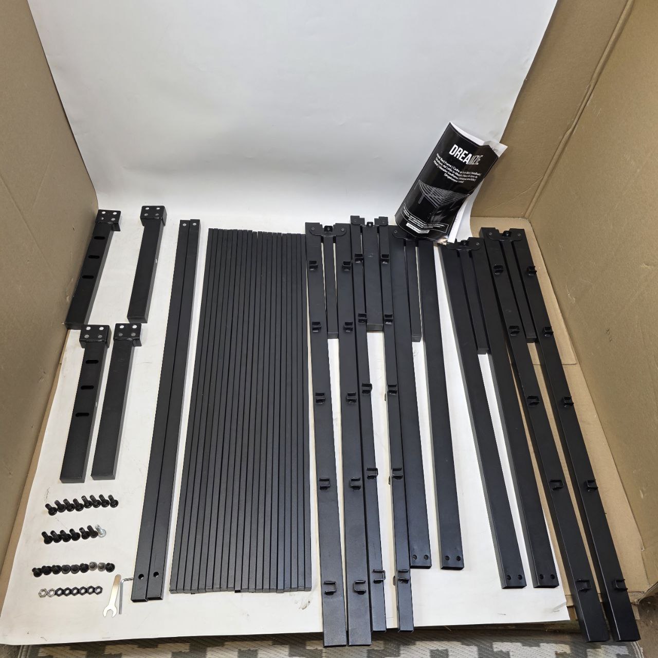 Set of black metal brackets and components on a white mat inside a cardboard box.