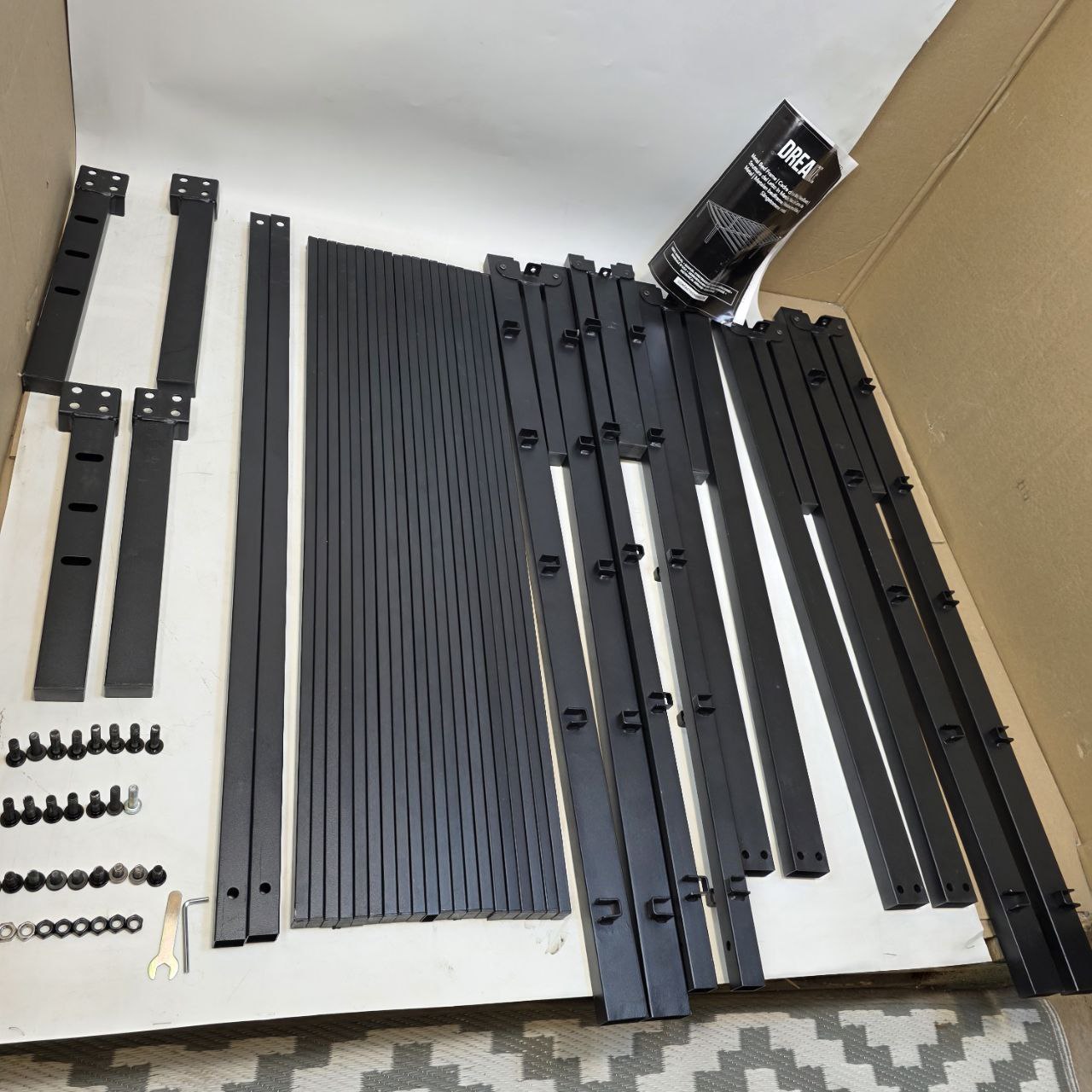 Black metal brackets and screws on a white surface with a cardboard box in the background.