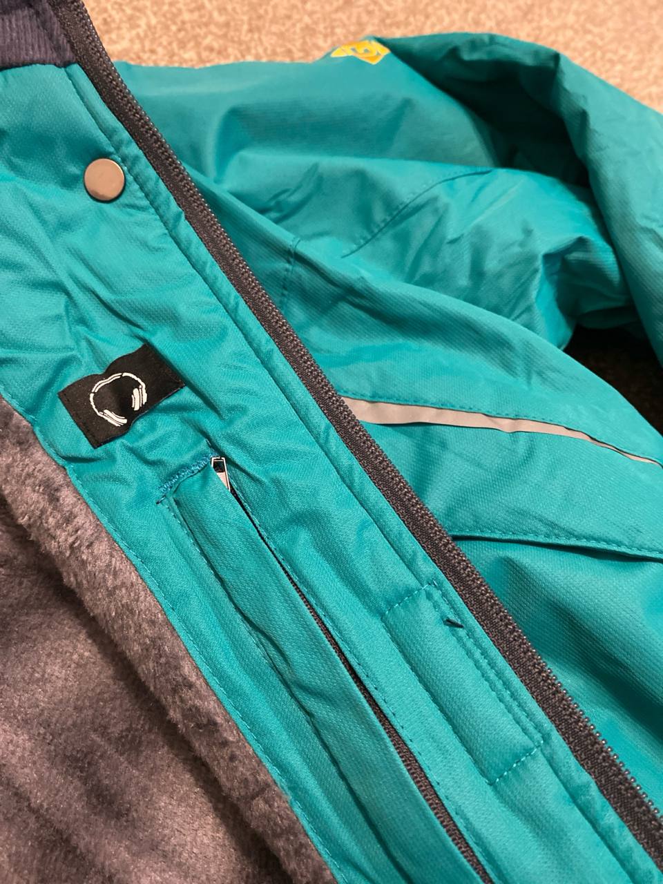 Teal jacket with a brand logo on the chest area.