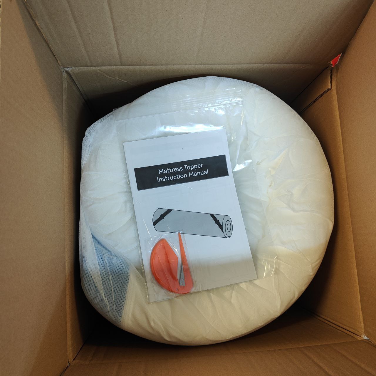 Mattress topper in a cardboard box with an instruction manual attached