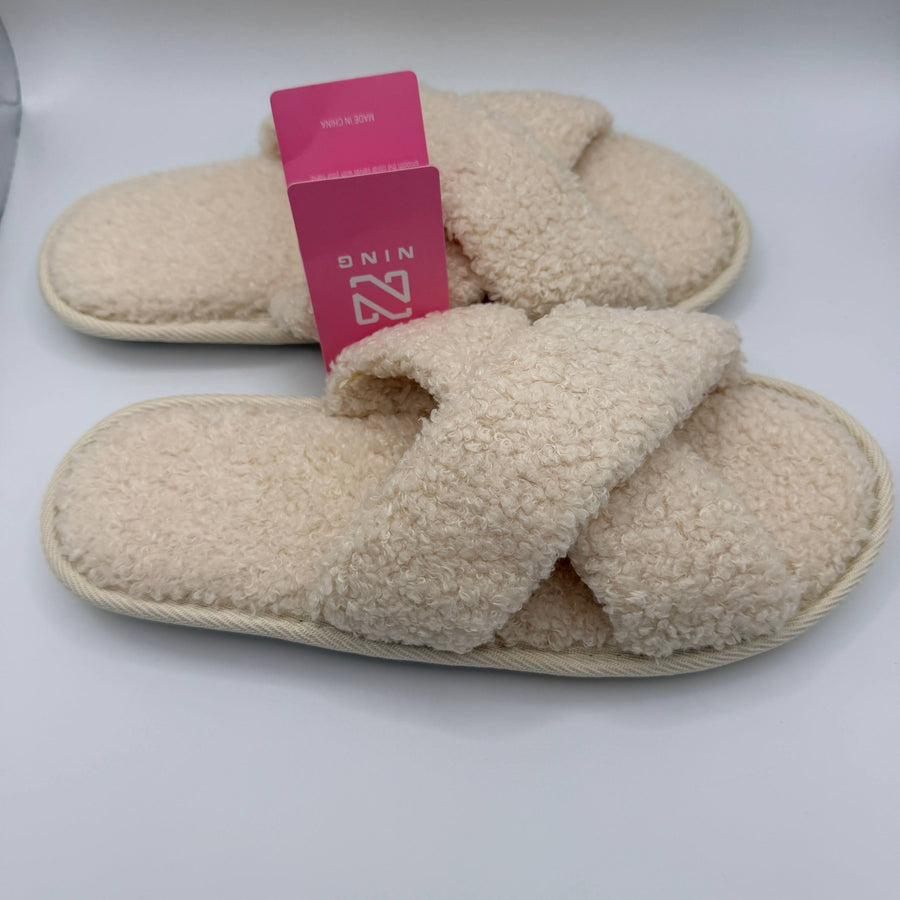 Pair of beige slippers with a pink tag on a white background