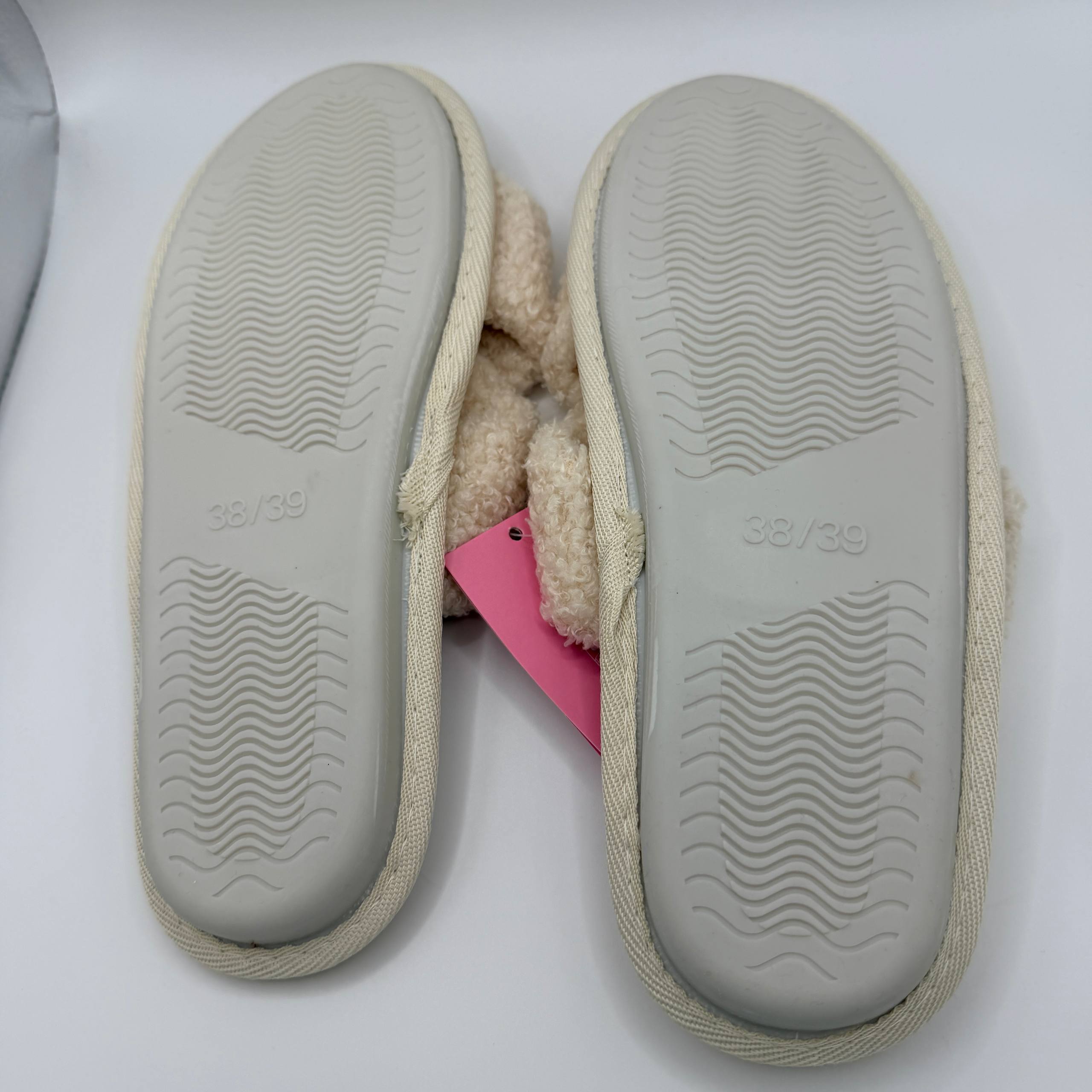 Pair of beige slippers with textured soles on a white background