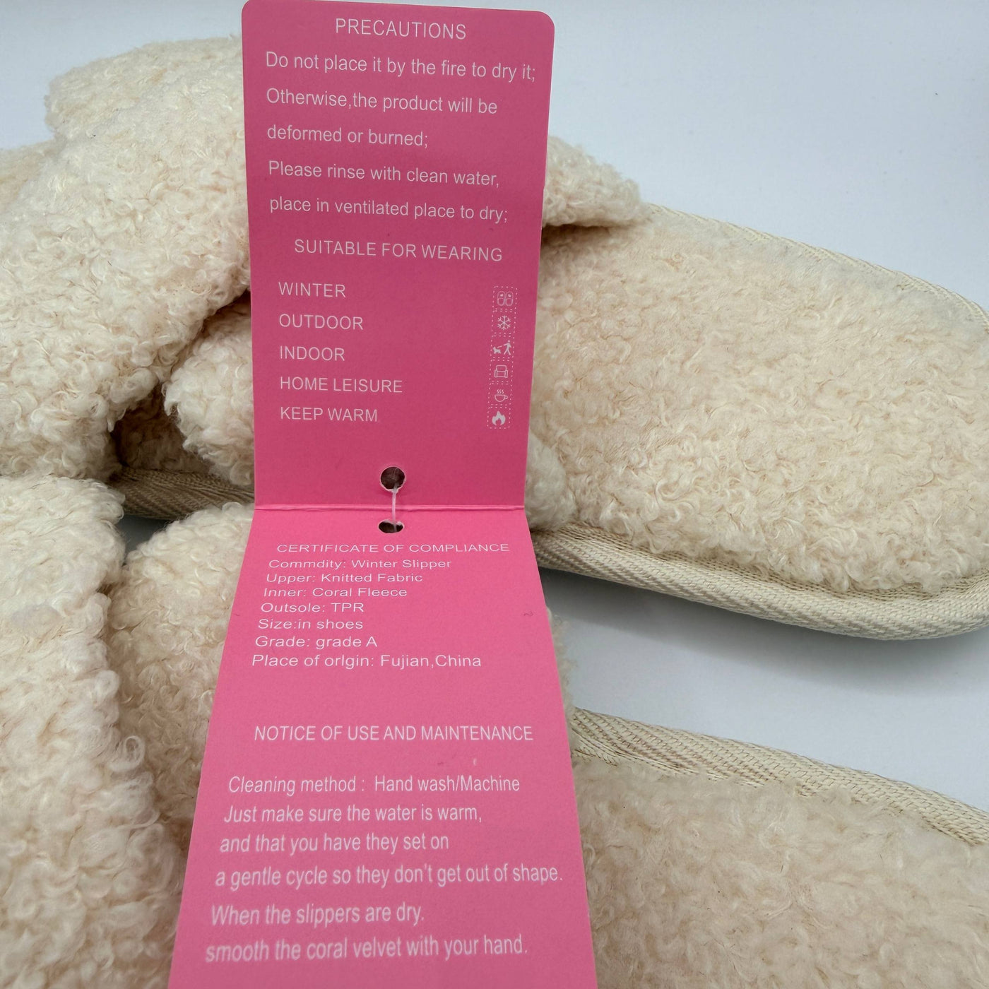 Beige slippers with a pink care label on a white background