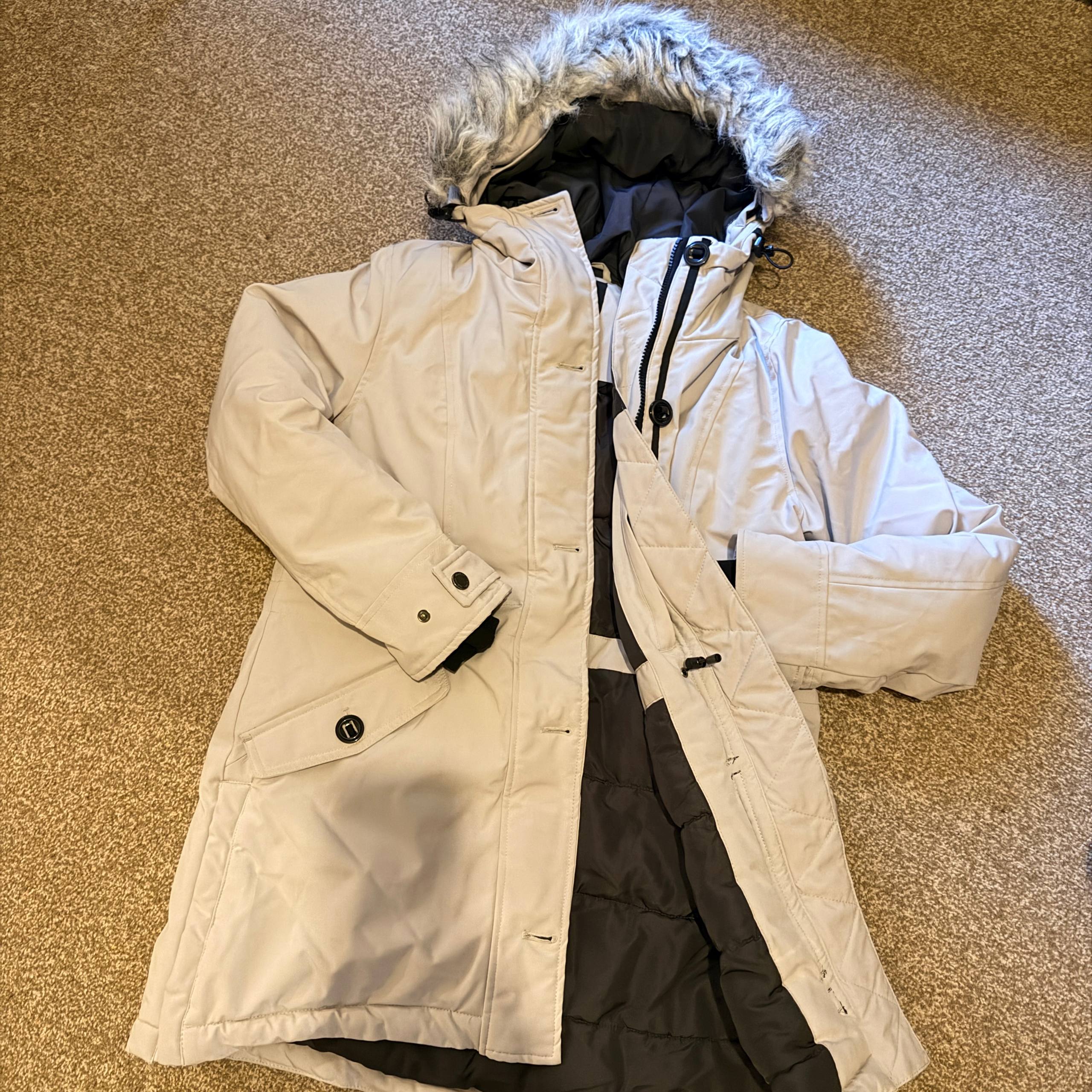 White winter coat with fur hood on a beige carpet