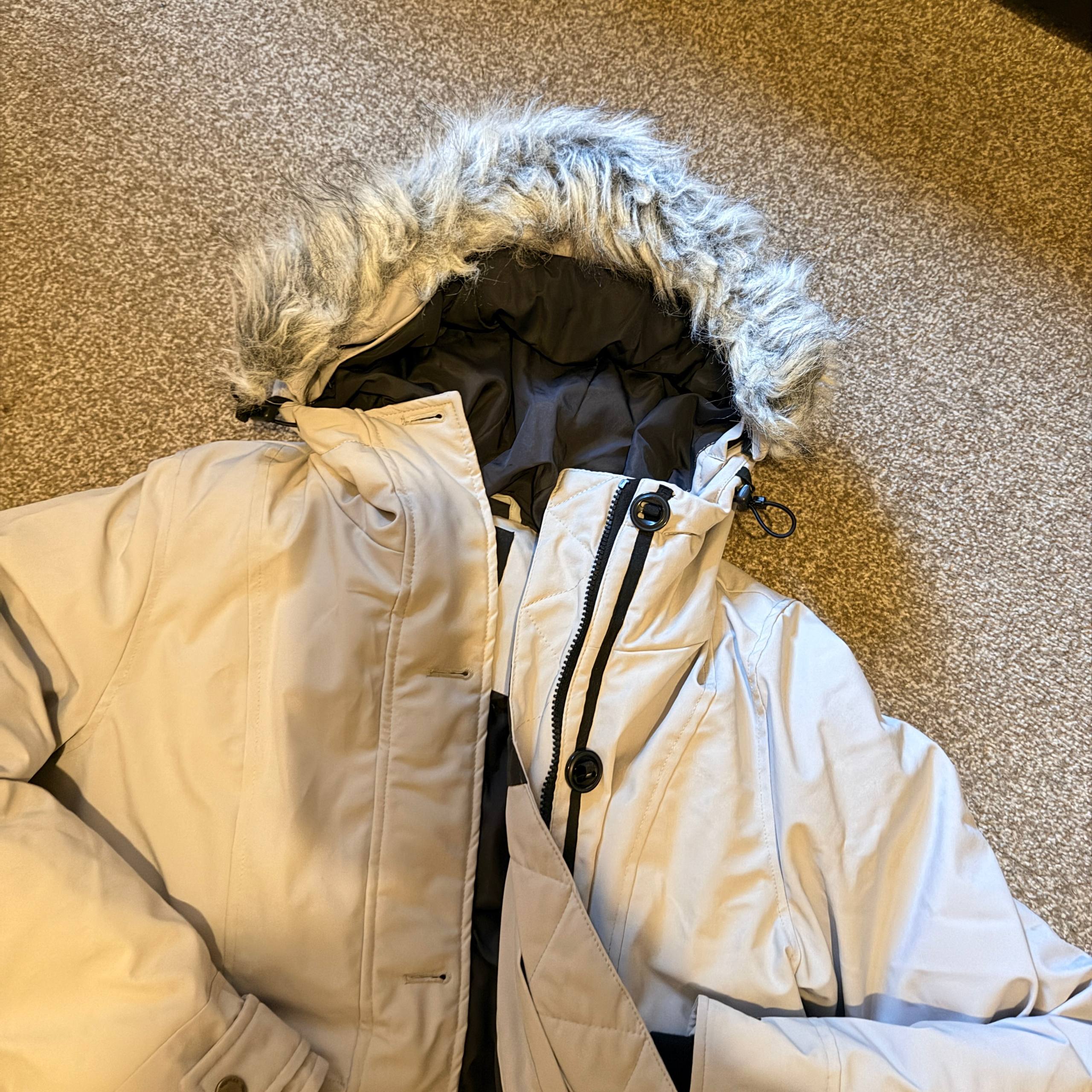 Beige winter coat with fur-lined hood on a textured surface