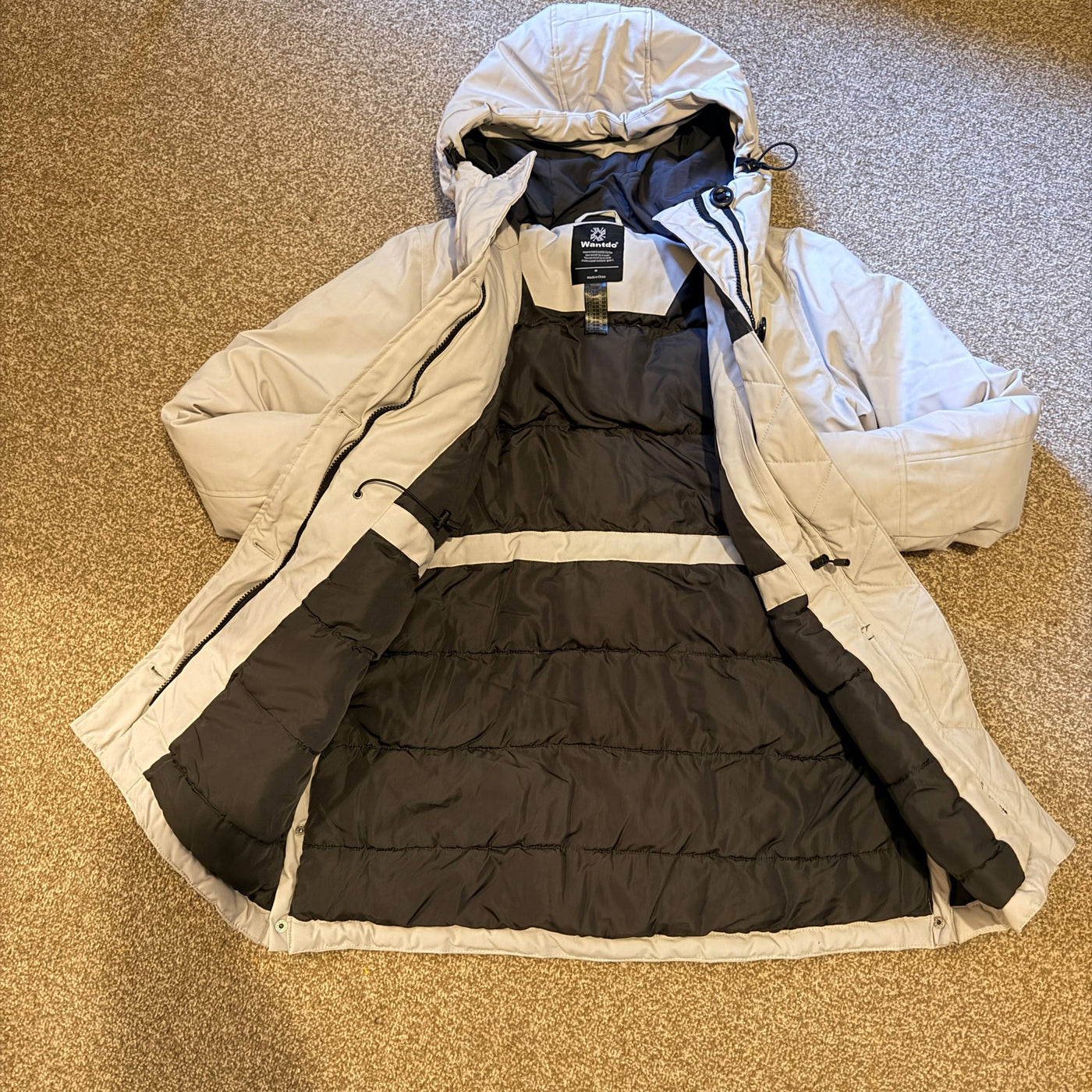 Two-layered puffer jacket with beige exterior and black interior on a textured surface