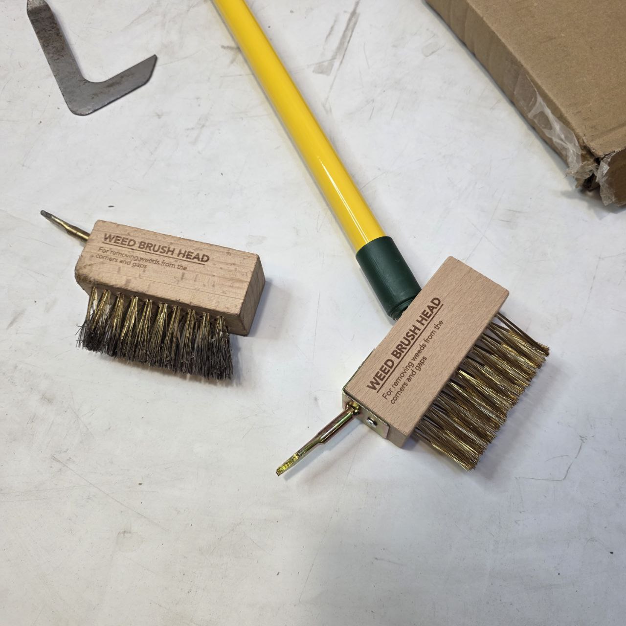 Two weed brush heads with a yellow handle on a white surface.