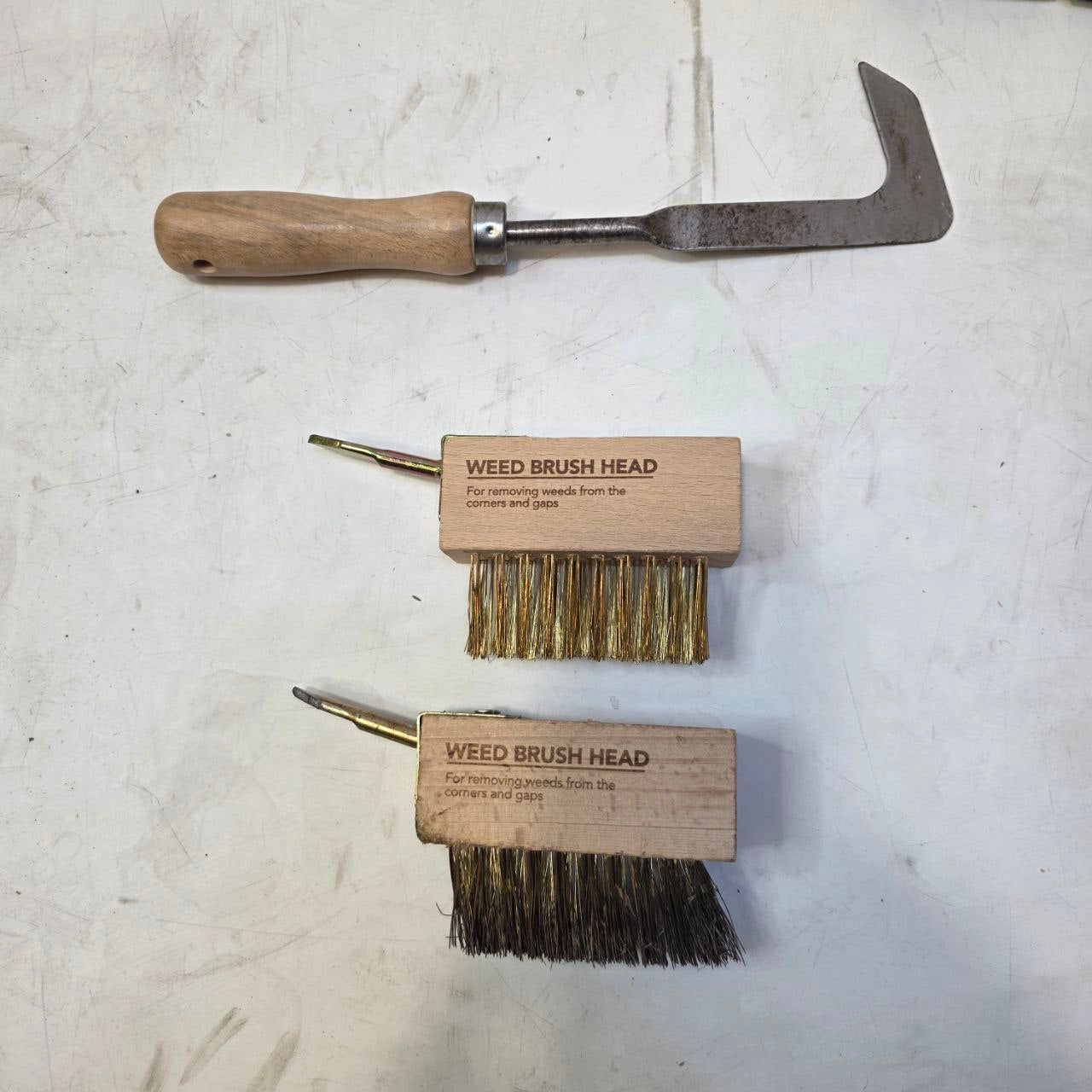 Set of gardening tools including a hook, two brush heads, and a chisel on a textured surface.