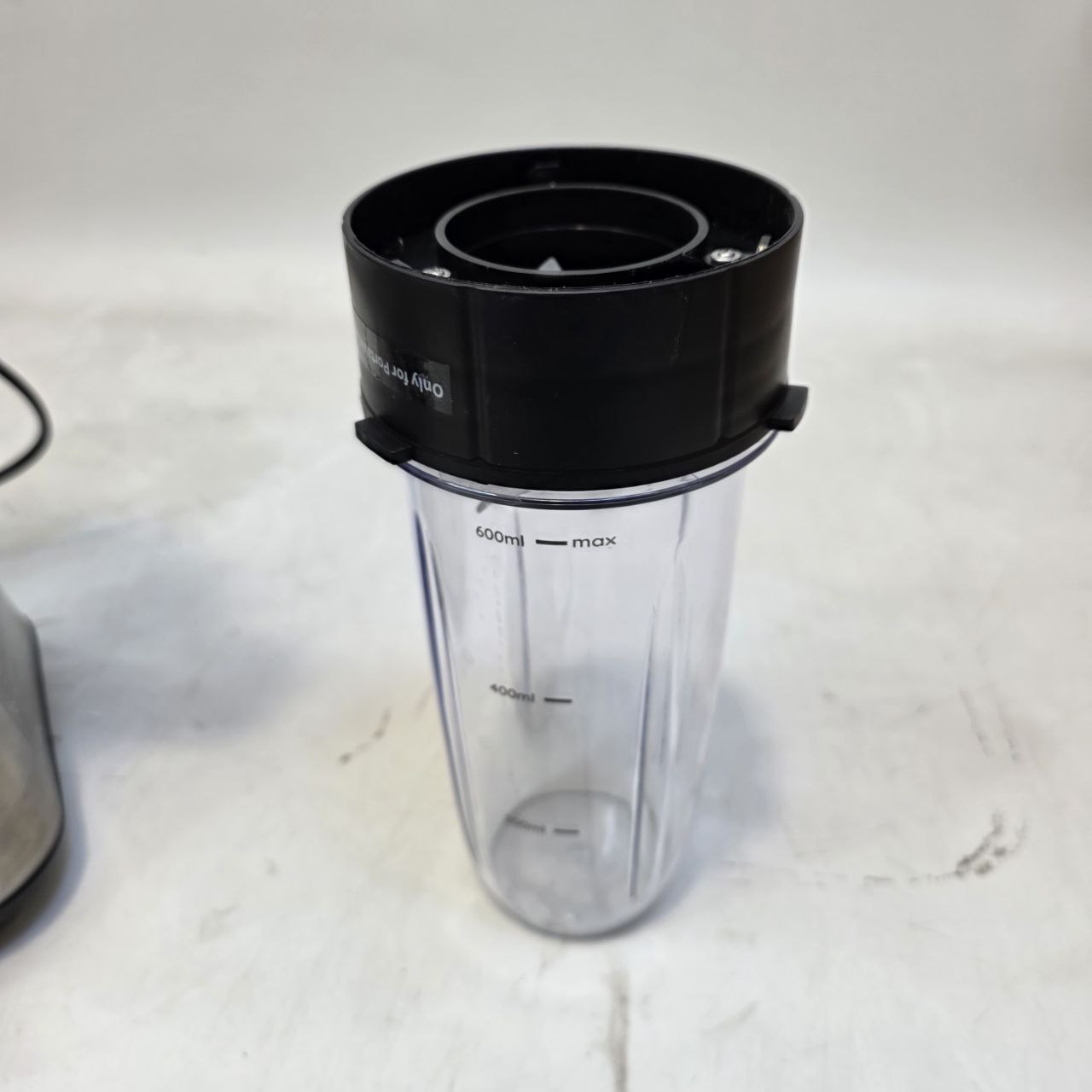 Clear blender container with black lid on a white surface