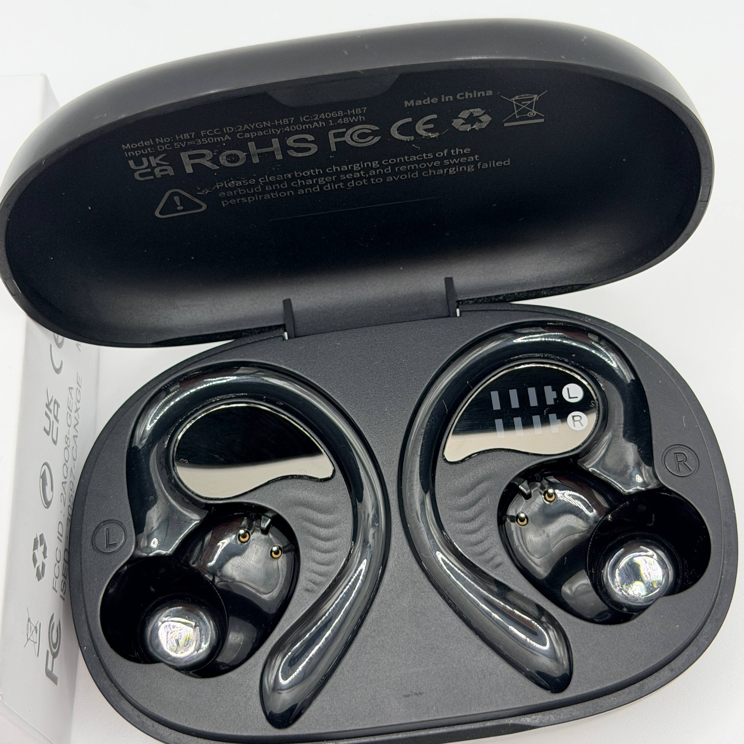 Black wireless earbuds in a charging case with visible branding and certification logos.