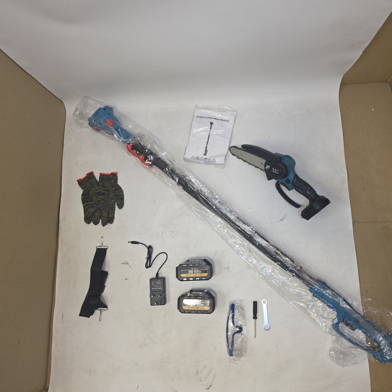 Gardening tools including a hedge trimmer, gloves, and batteries on a white surface.