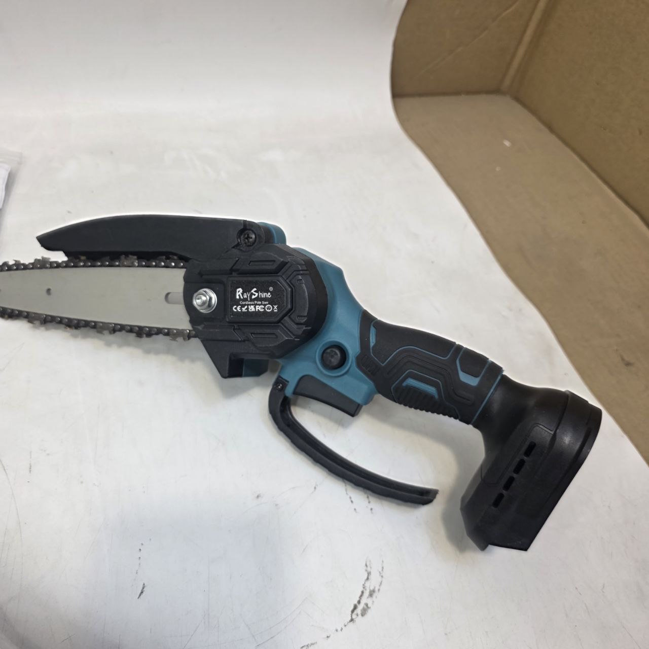 Handheld chainsaw on a white surface with a cardboard box in the background