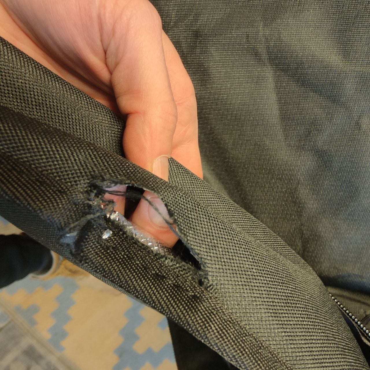 Hand holding a worn-out section of a jacket with visible stitching and fabric texture.