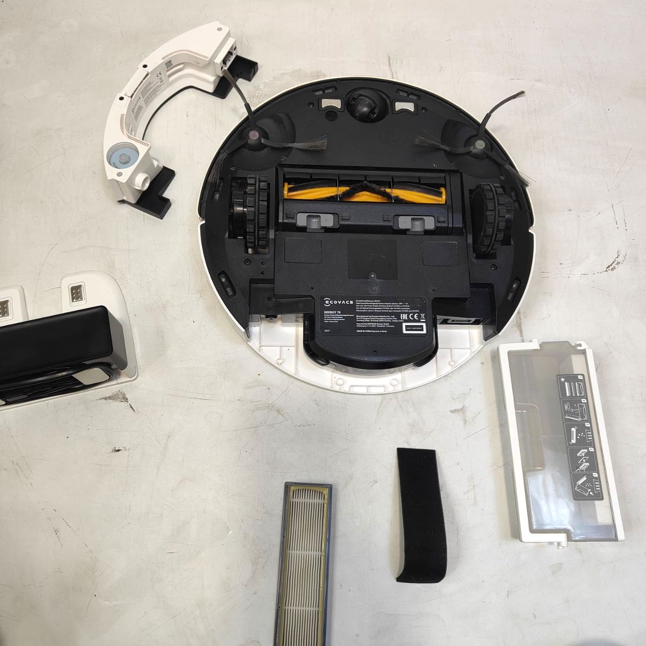 Disassembled robot vacuum cleaner on a light gray surface with various parts scattered around.