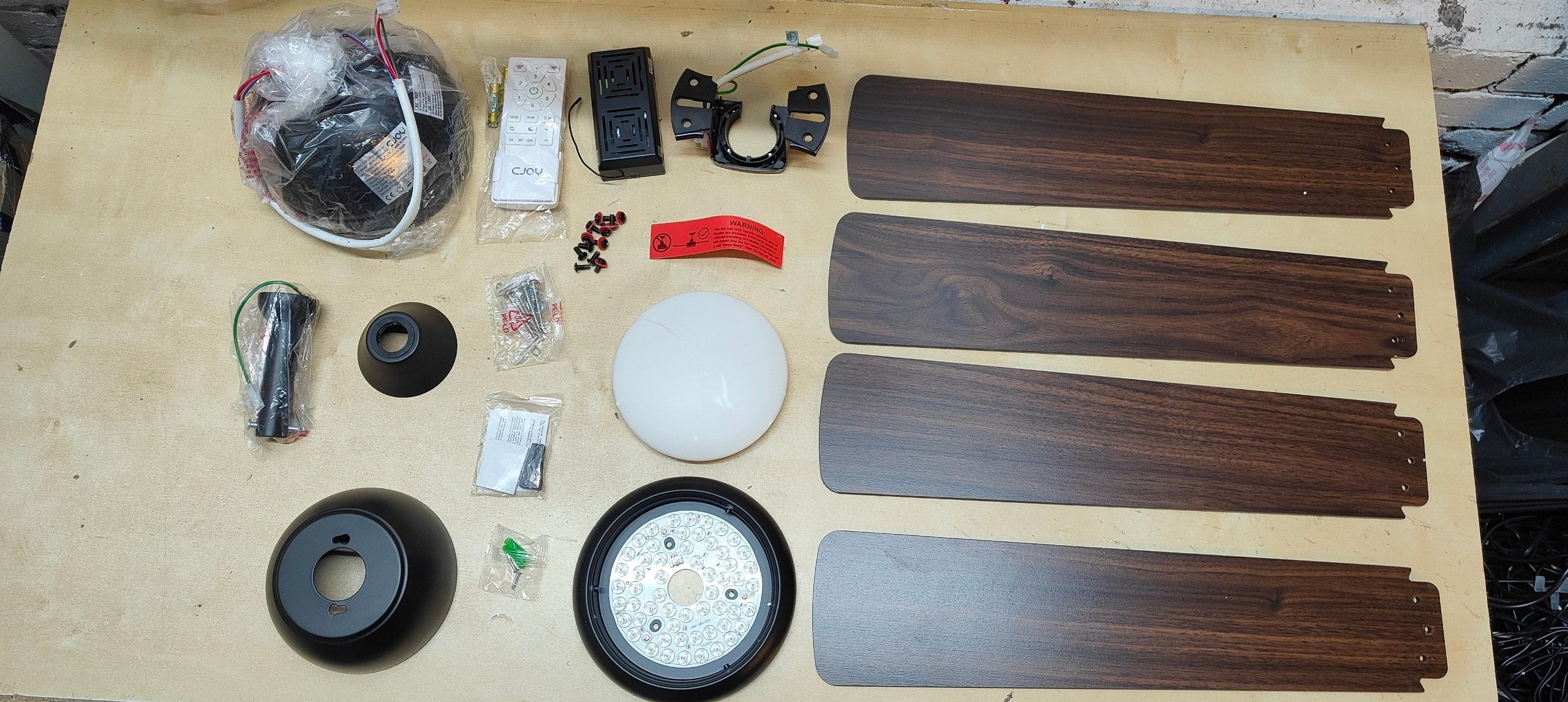 Collection of ceiling fan parts including blades, motors, and other components on a wooden surface.