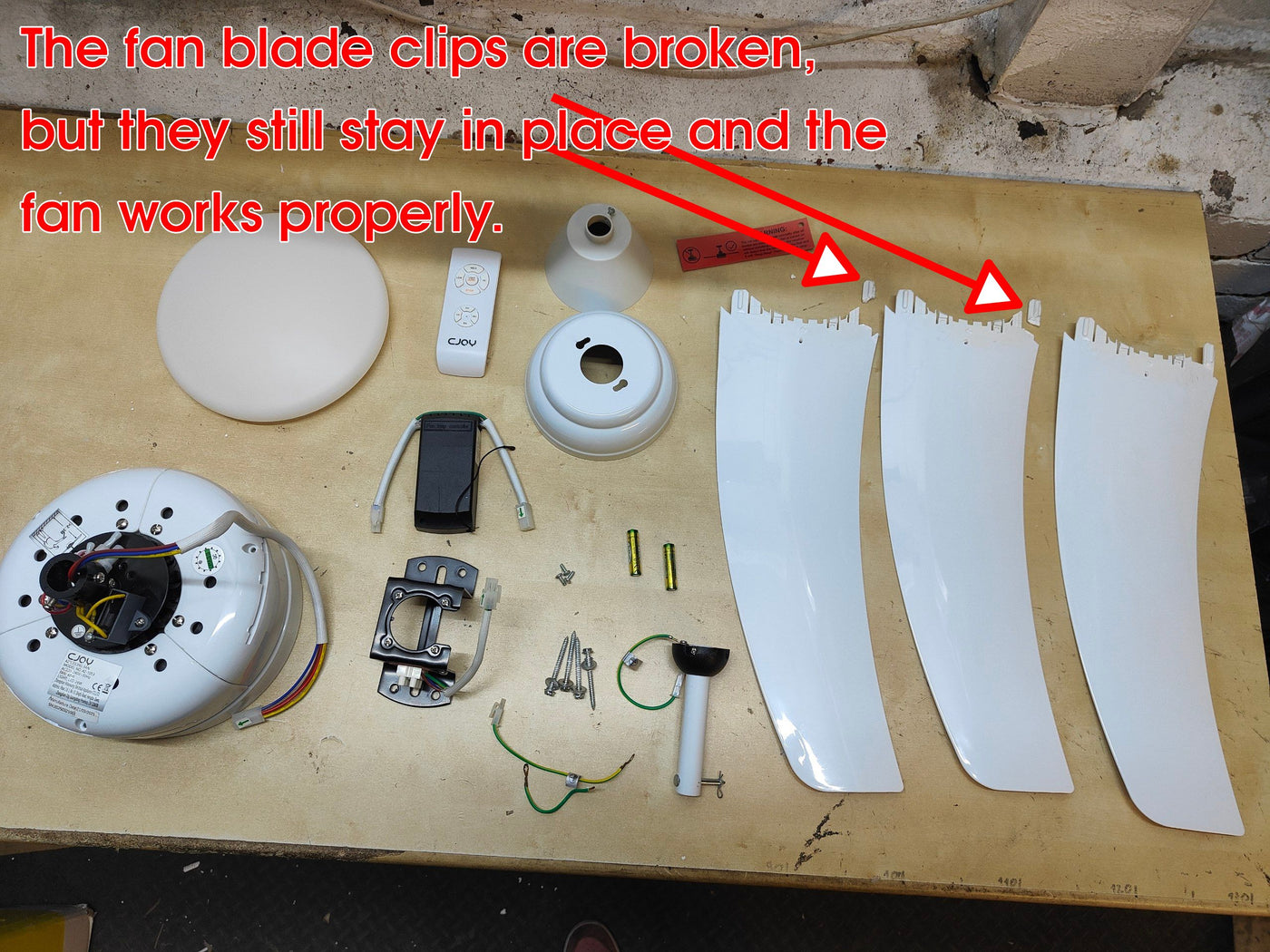 Fan parts on a wooden surface with text indicating broken clips but proper functioning.