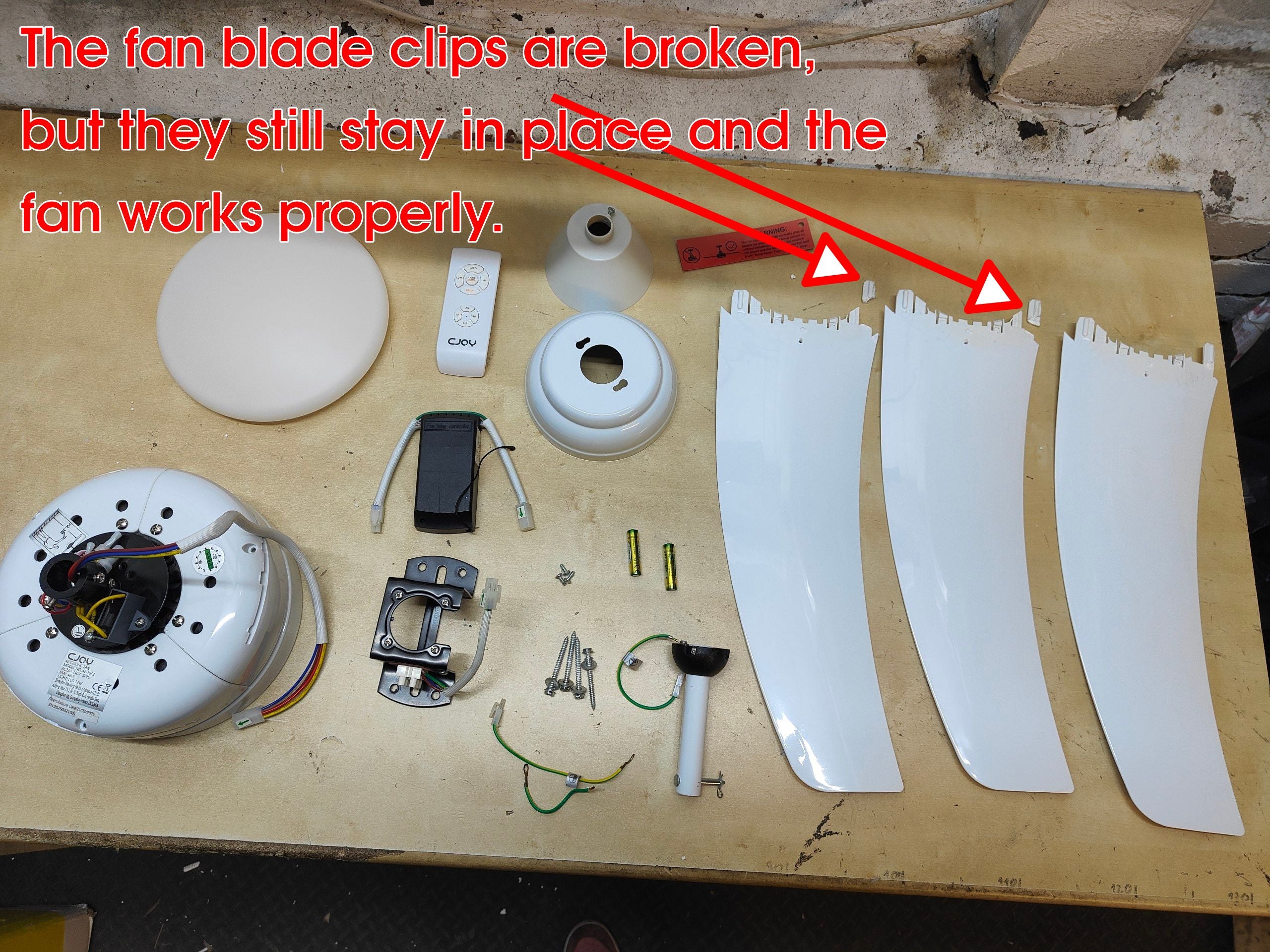Fan parts on a wooden surface with text indicating broken clips but proper functioning.