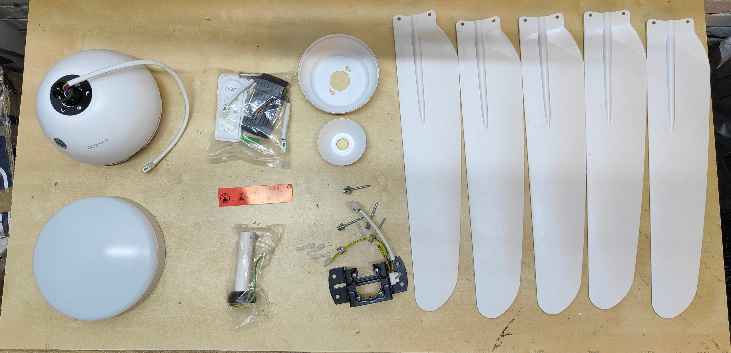 Ceiling fan parts including blades, motor housing, and mounting hardware on a wooden surface.