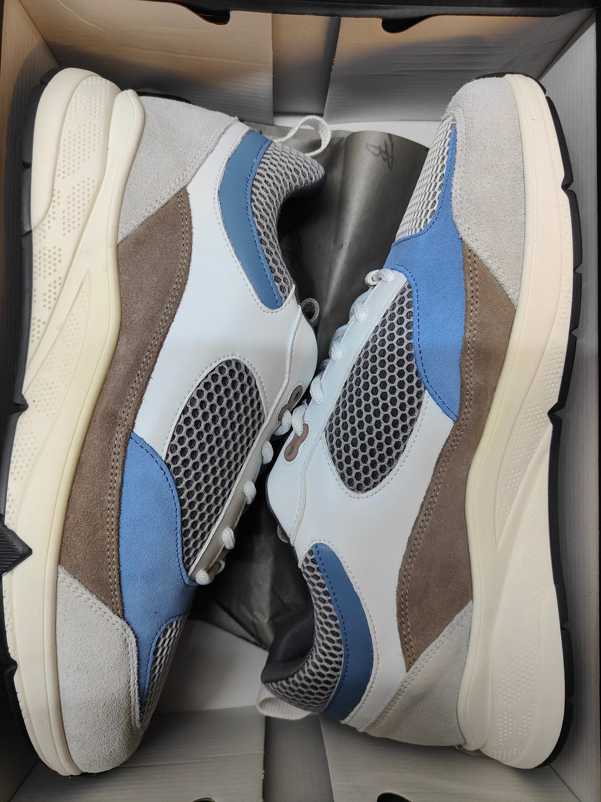 Pair of sneakers with a mix of gray, blue, and white colors in a box.